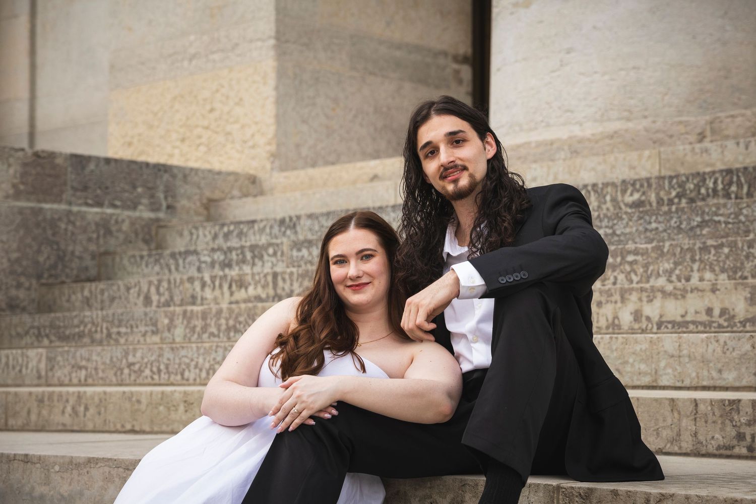 A couple shares happy moments while posing against an architectural backdrop with stone columns.