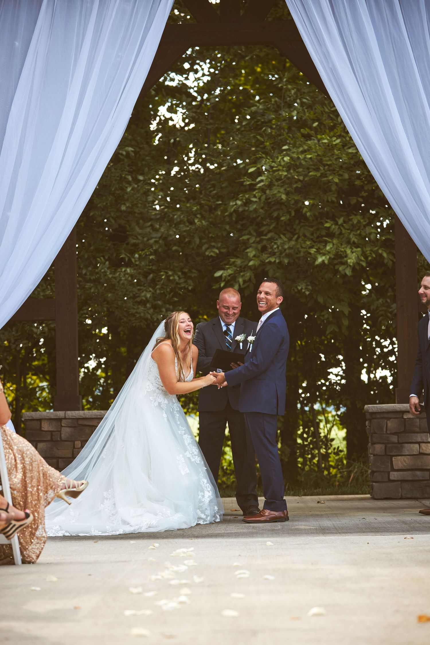 An outdoor wedding ceremony under white draped fabric and trees.
