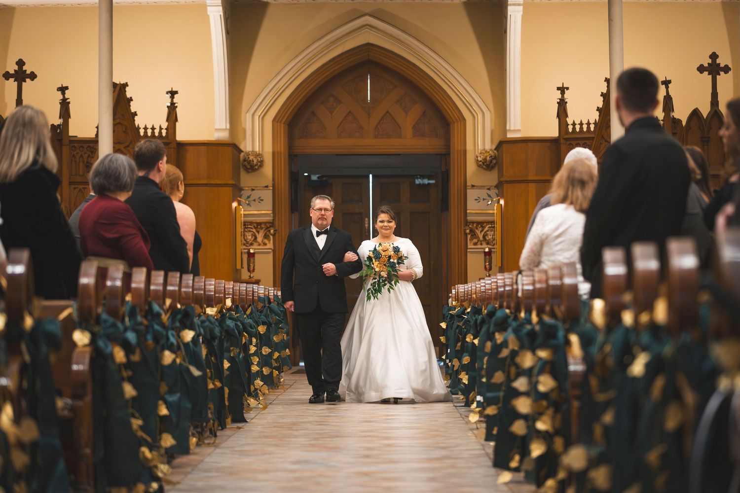 Church aisle decorated with yellow floral arrangements and pew bows during wedding ceremony.