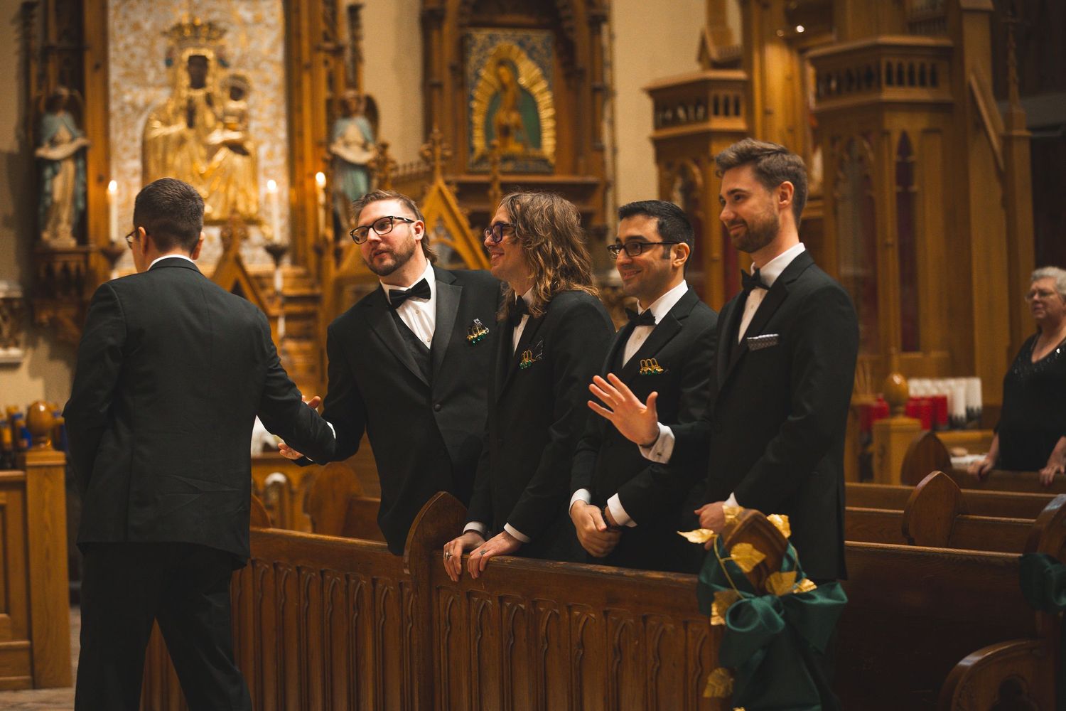 Groomsmen share a lighthearted moment inside an ornate church with gothic architecture and religious artwork.
