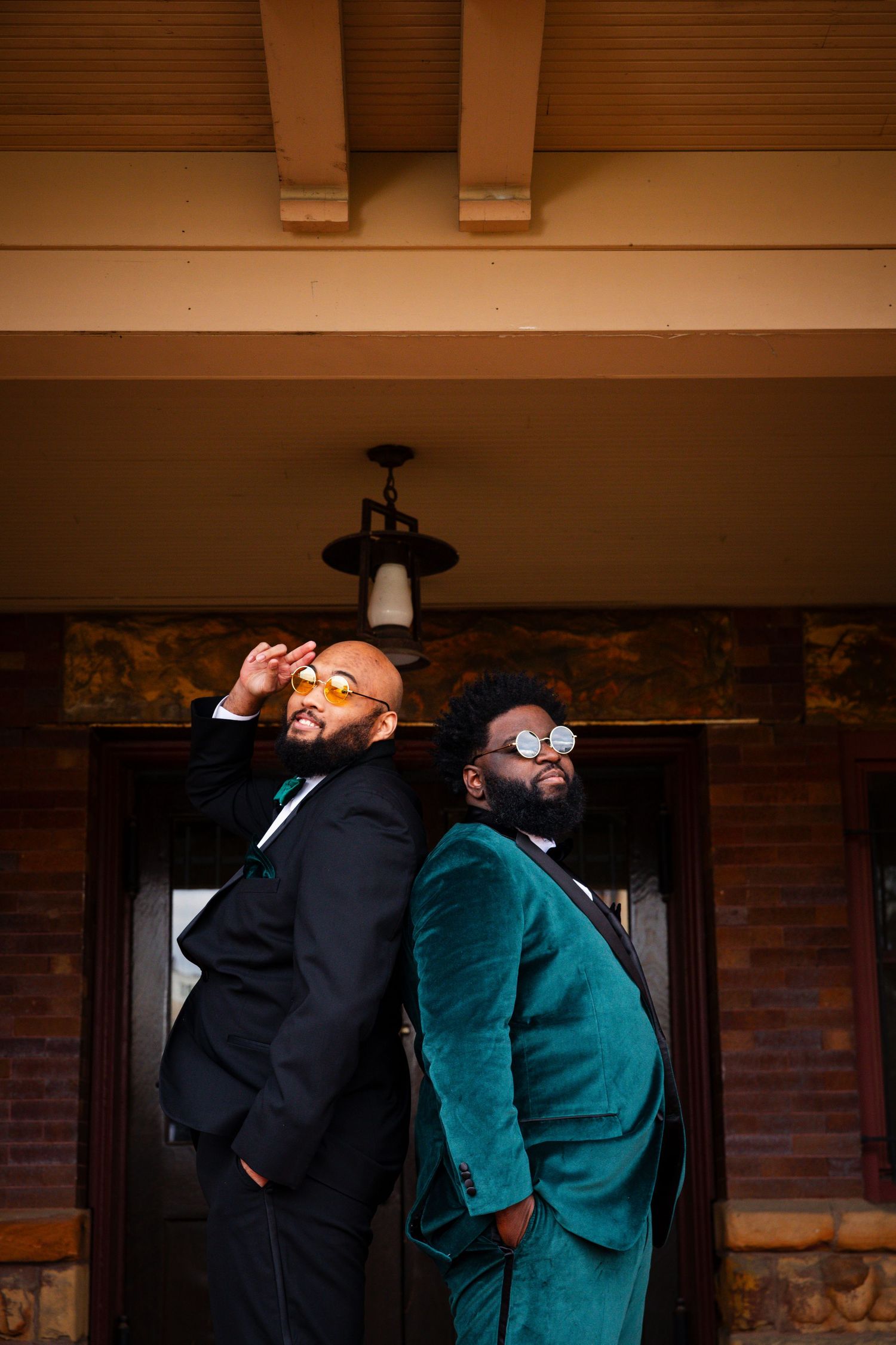 Wedding party members in emerald and black suits share animated moments outside venue.