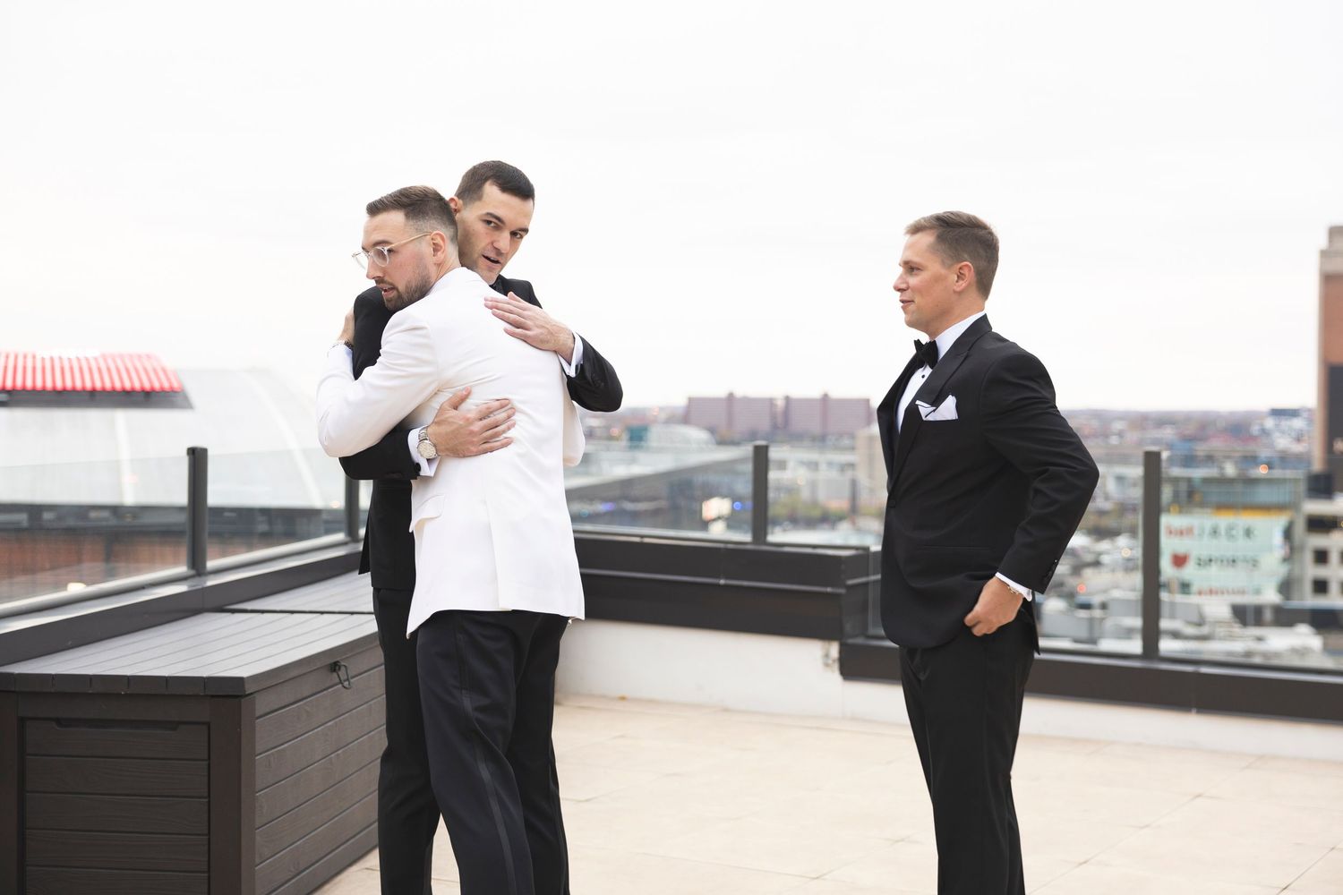 People in formal attire greet each other on an outdoor terrace with city views.