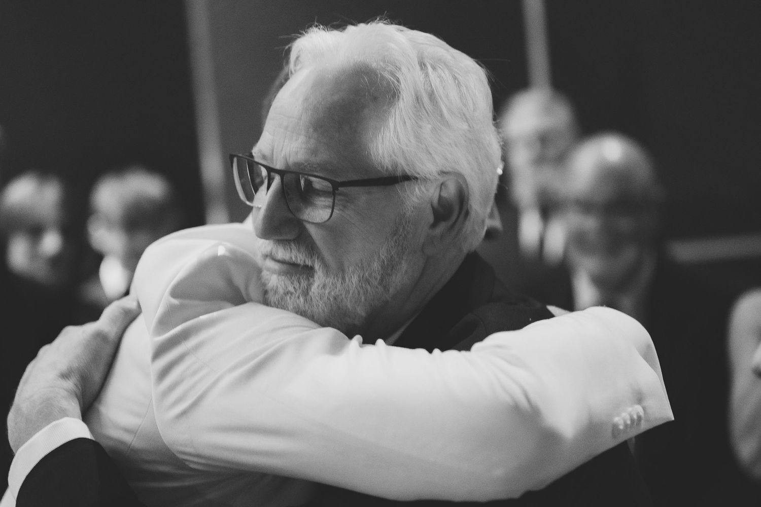 Guests embrace in an emotional moment during a formal event in a dark venue.