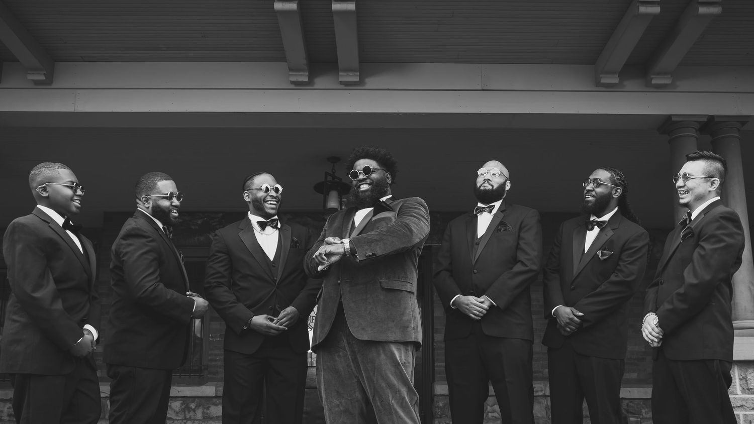 Wedding party lined up in formal attire outside a building in panoramic view.