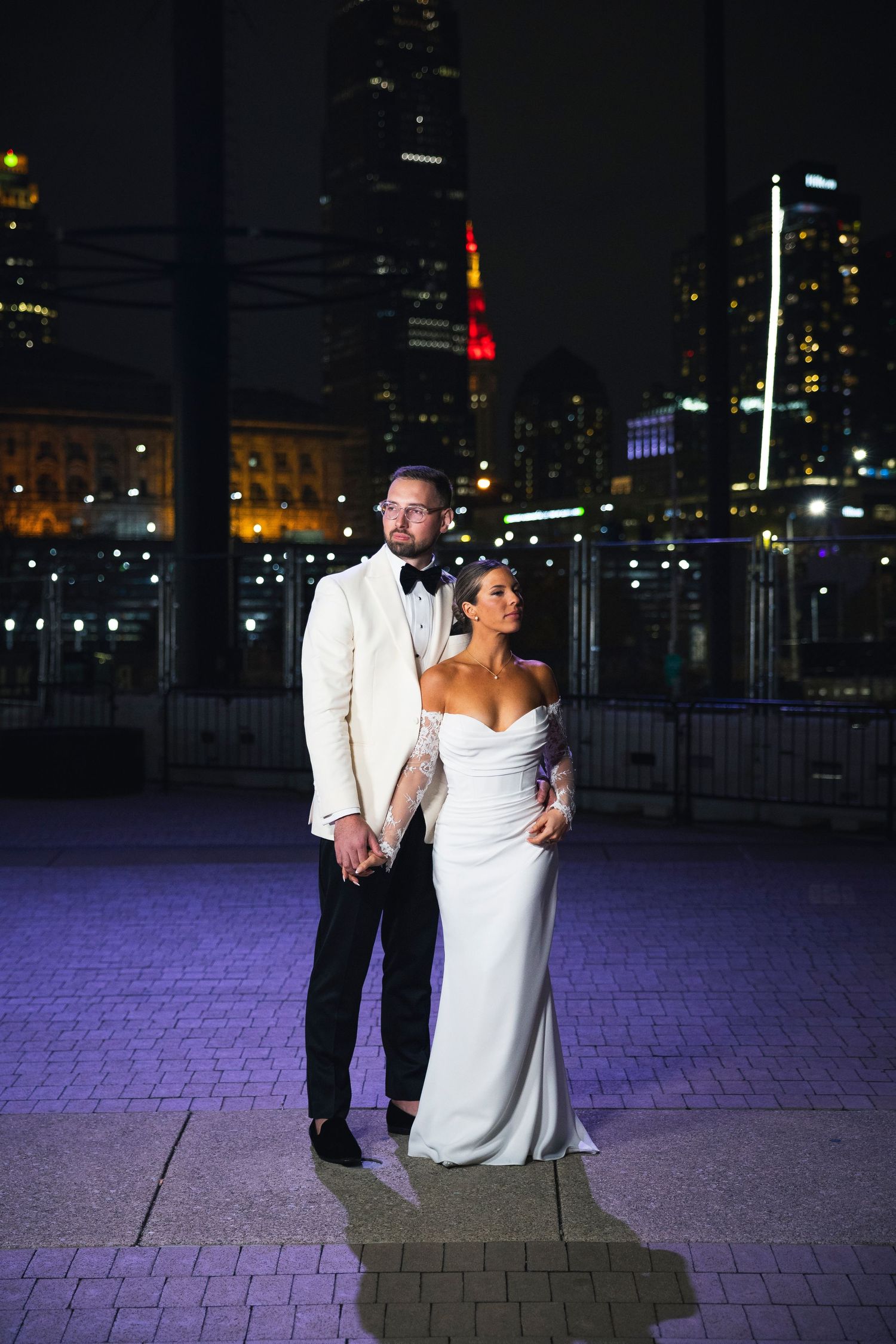 A romantic nighttime portrait with illuminated skyscrapers and purple ambient lighting.
