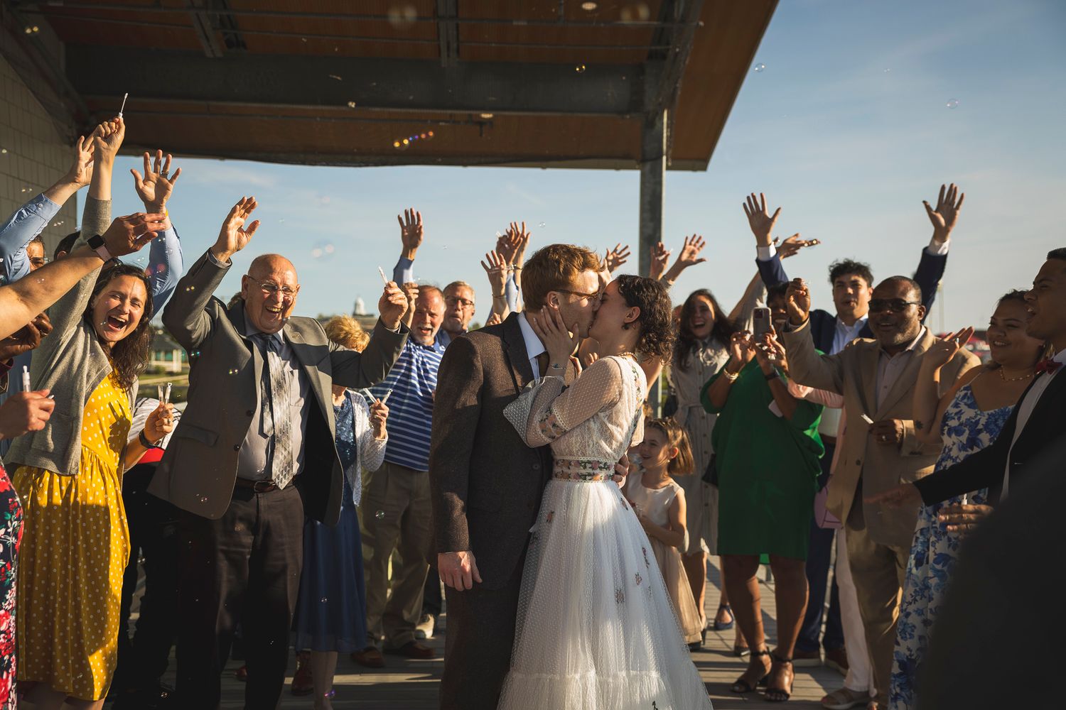 Wedding guests celebrate with raised arms under an outdoor pavilion during a joyful reception.