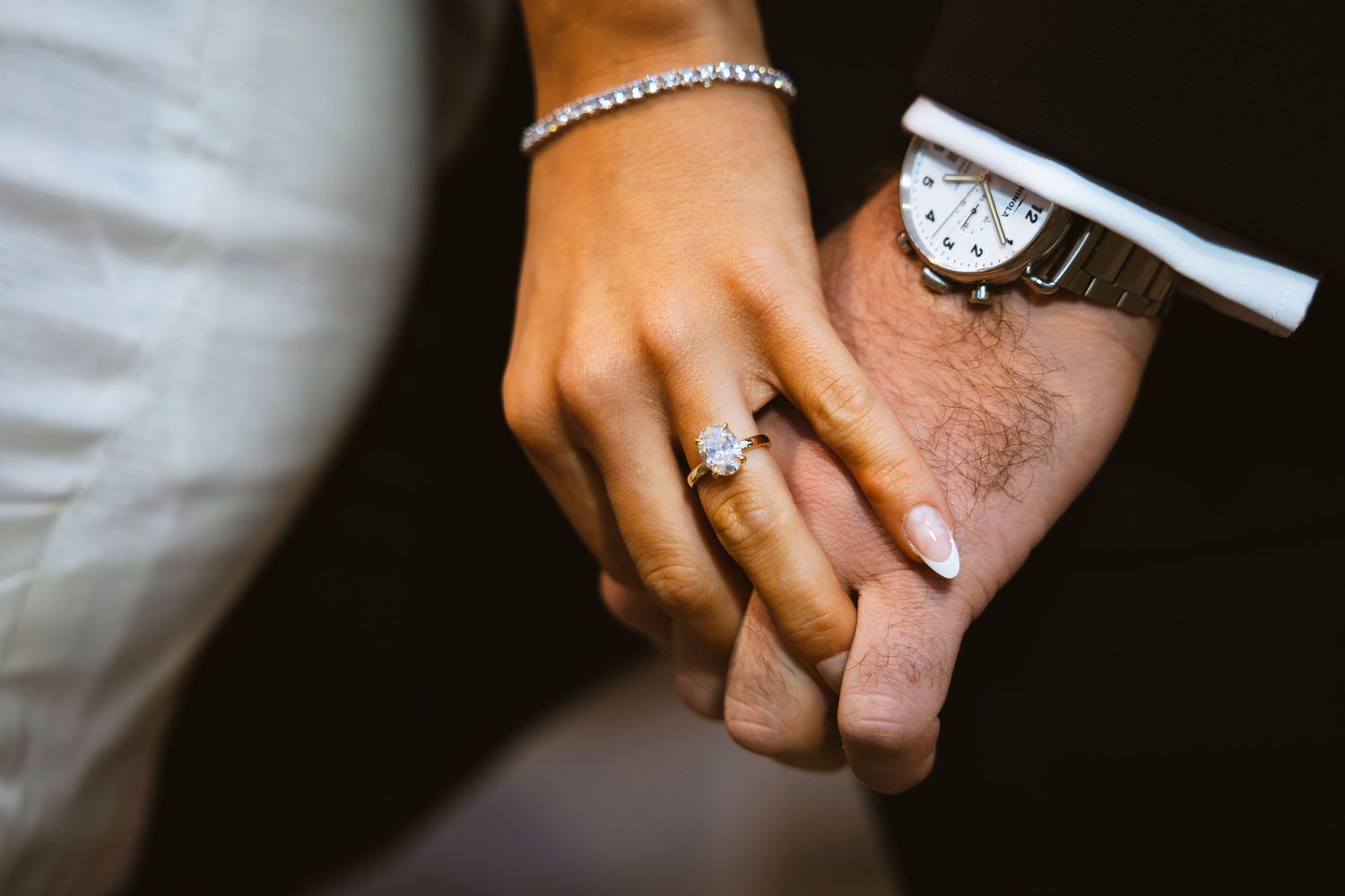 Multiple hands wearing elegant jewelry and rings shown in detail against a dark background.