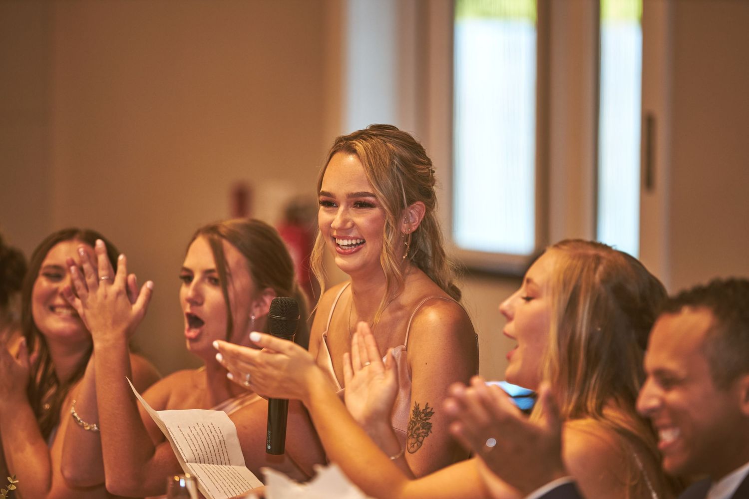 Wedding guests laugh and react emotionally during a reception celebration.