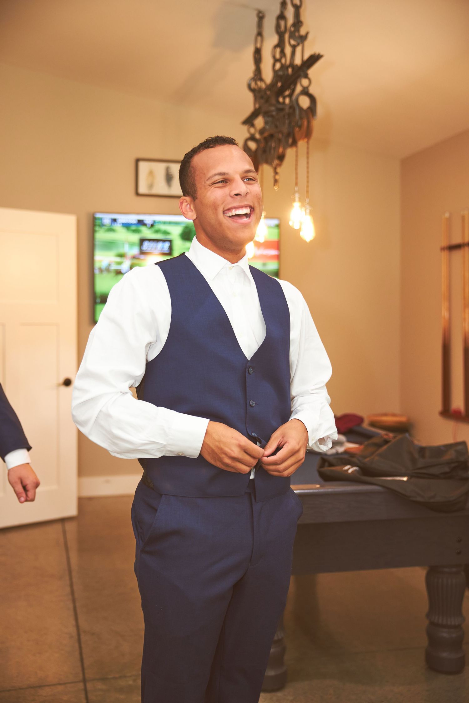 Wedding party member in navy vest and white shirt getting ready indoors.