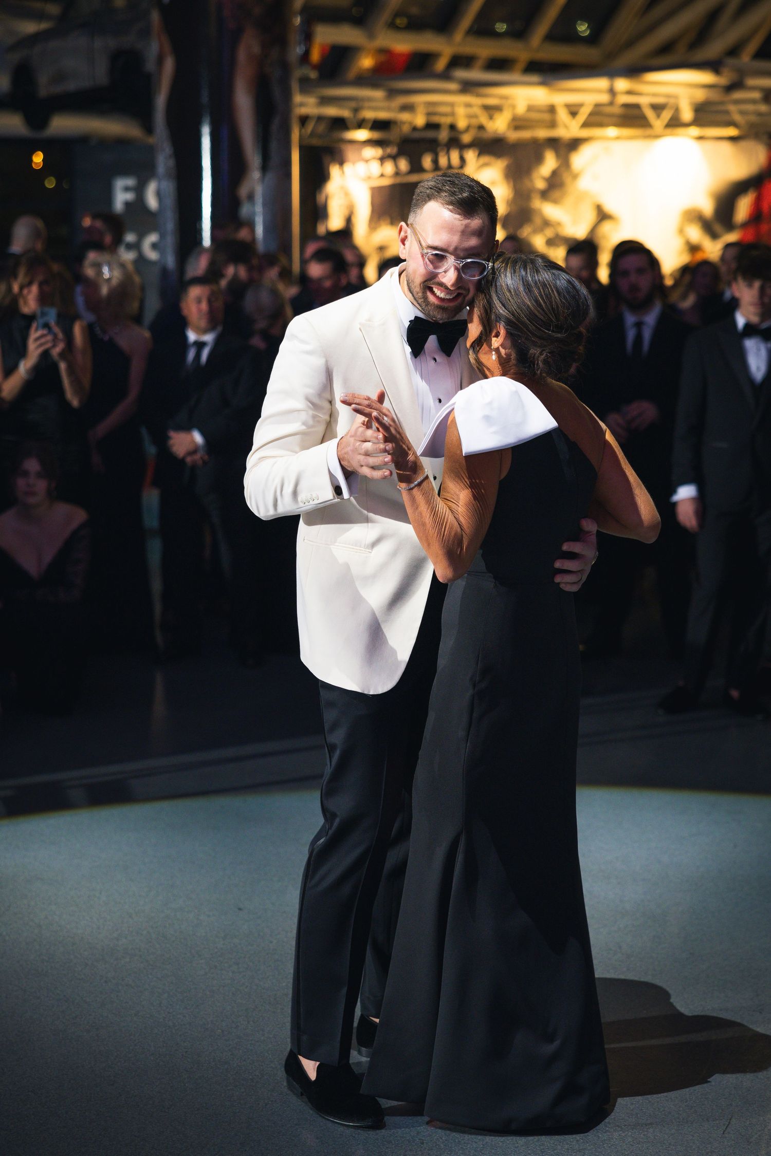 Two people share an intimate dance at an elegant evening reception with warm lighting.