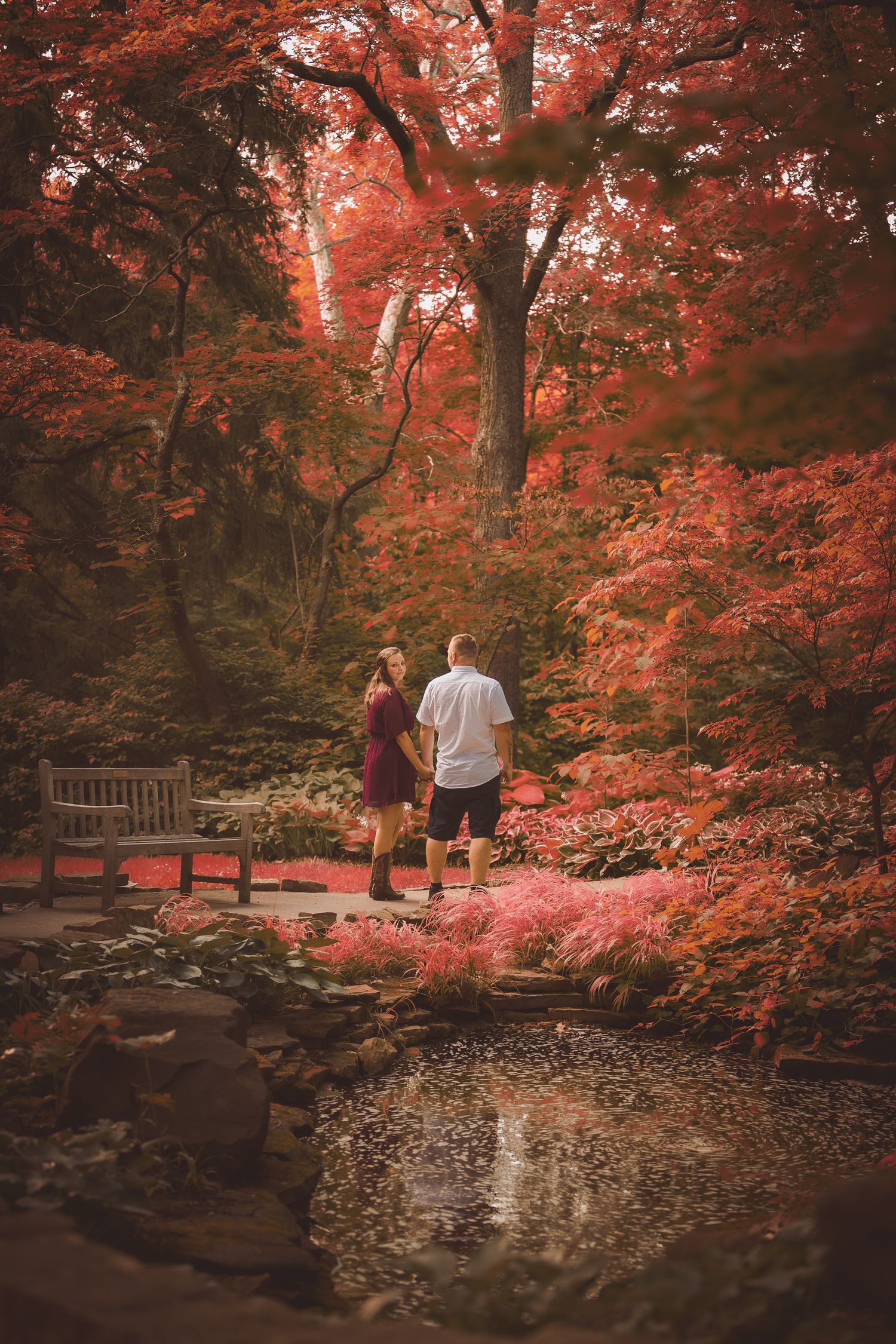 A scenic garden path with vibrant red Japanese maple trees and a reflecting pond.