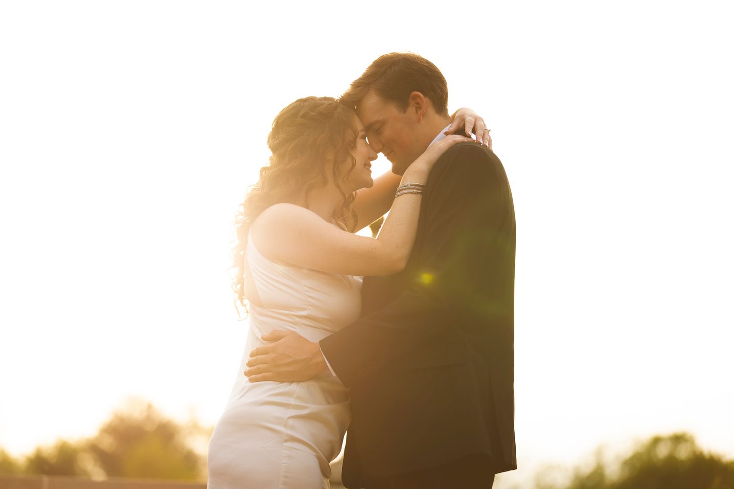 Couple shares intimate moment in glowing golden sunlight during outdoor wedding portrait.
