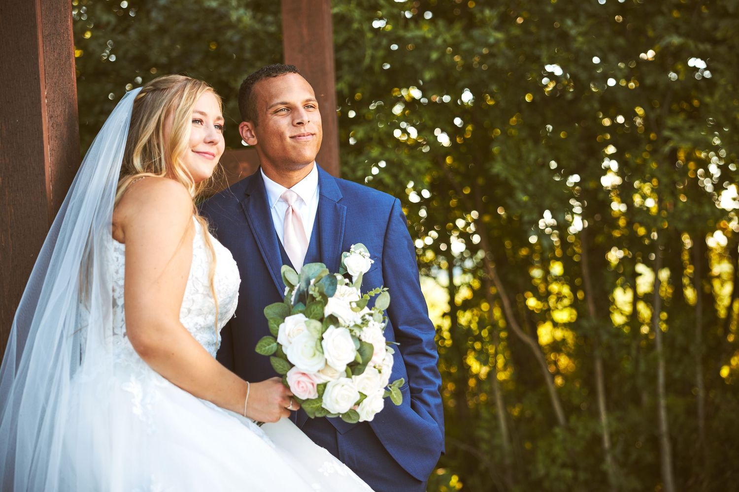 Romantic wedding portrait with white drapes and lush greenery in golden sunlight.