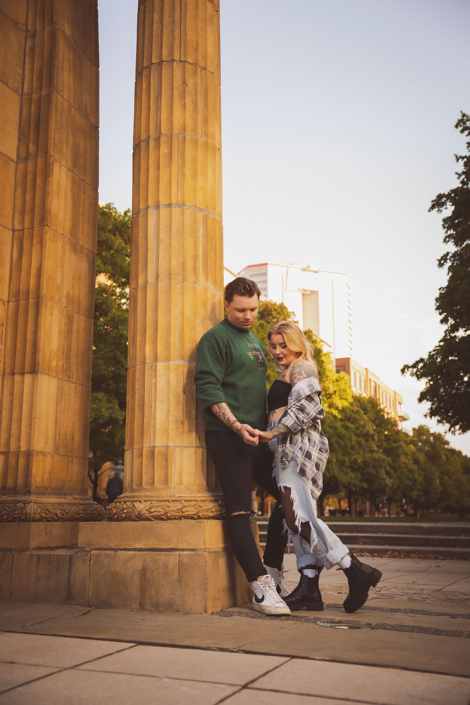 Couple shares an intimate moment between classic stone columns at sunset.