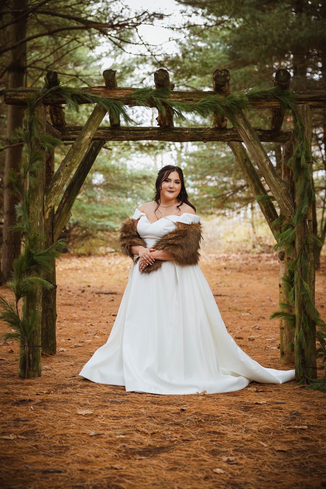Bride in white dress posing under rustic wooden pergola in forest setting.