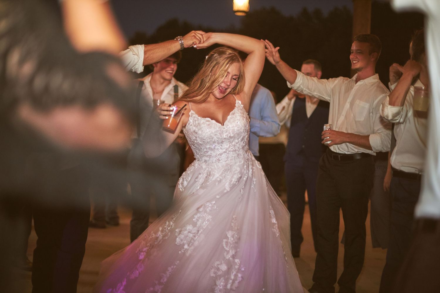 A bride twirls in her sparkly white wedding gown on the dance floor surrounded by party guests.