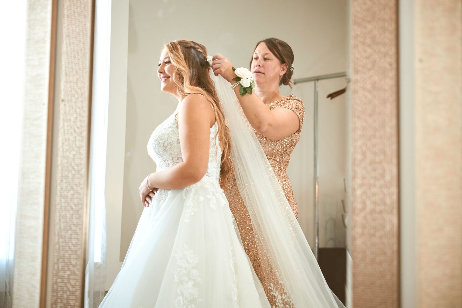 Final wedding dress preparations with attendant adjusting bride's veil.
