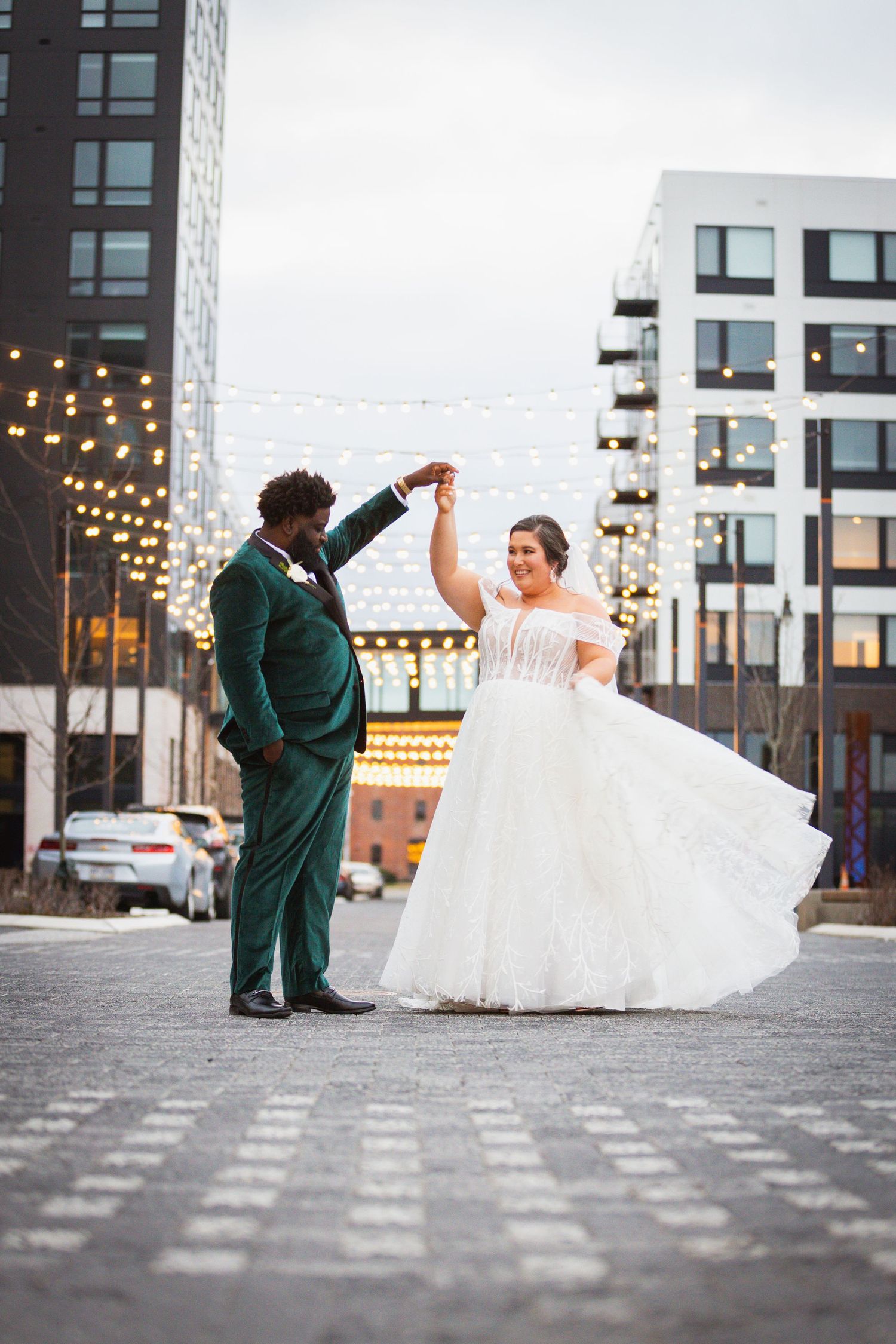Dance sequence on city street with string lights and modern architecture.