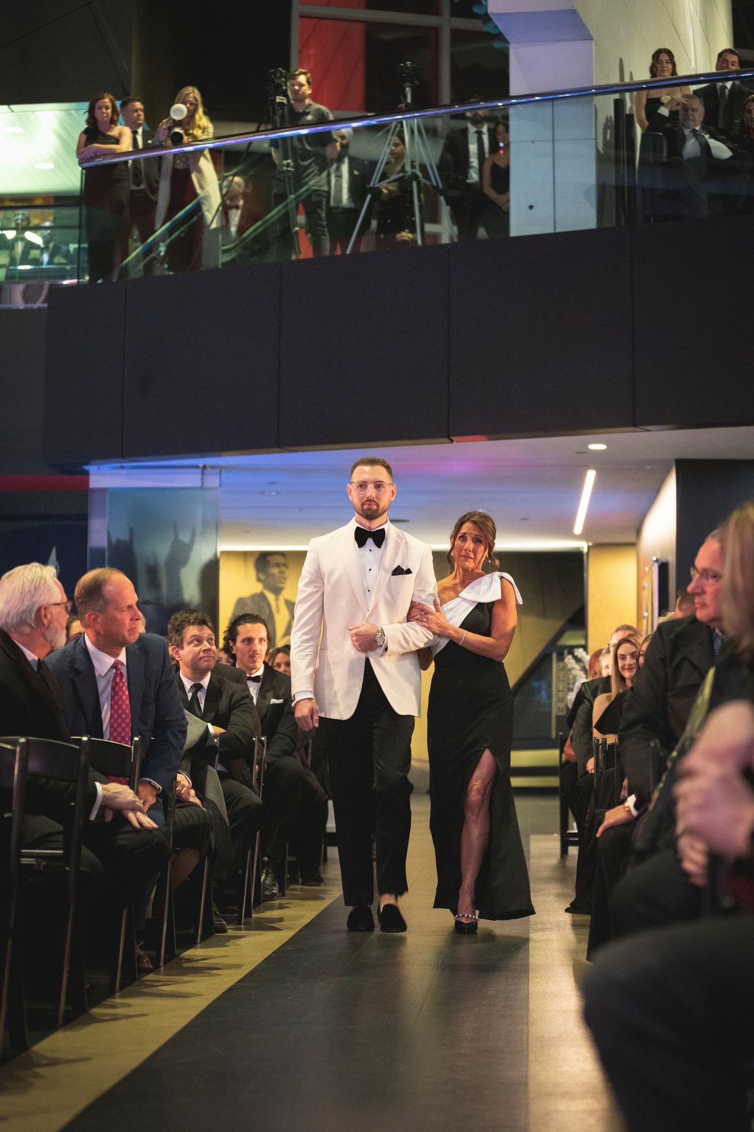 Wedding guests watching ceremony from balcony in formal attire.