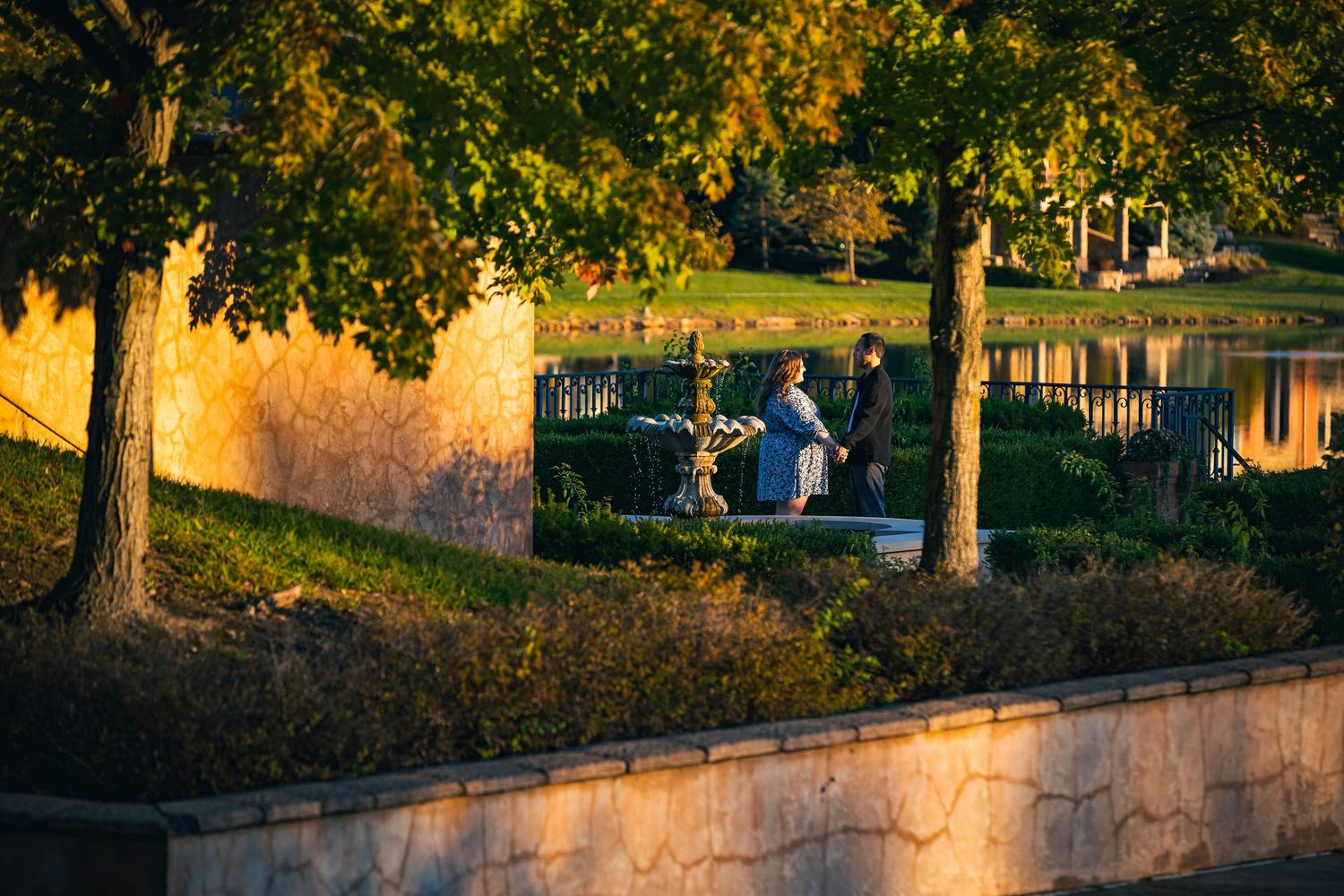 A couple walks together on a stone path during golden hour with trees and autumn foliage.