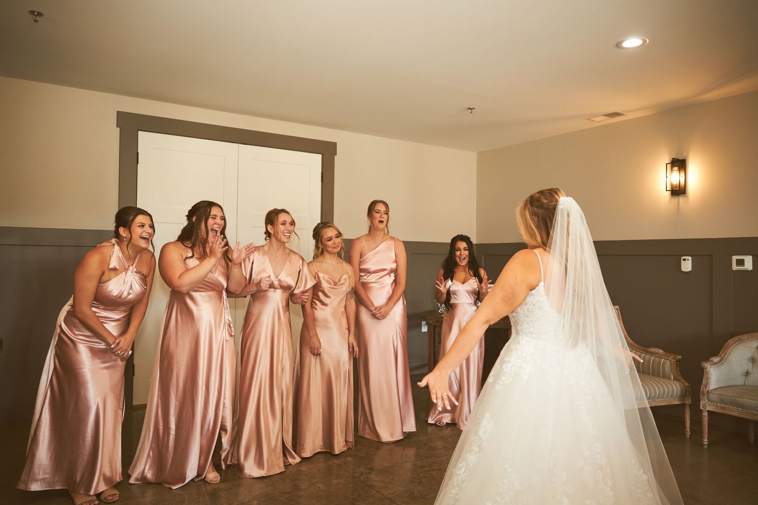 Bridesmaids in rose gold satin dresses watching bride in her wedding gown.