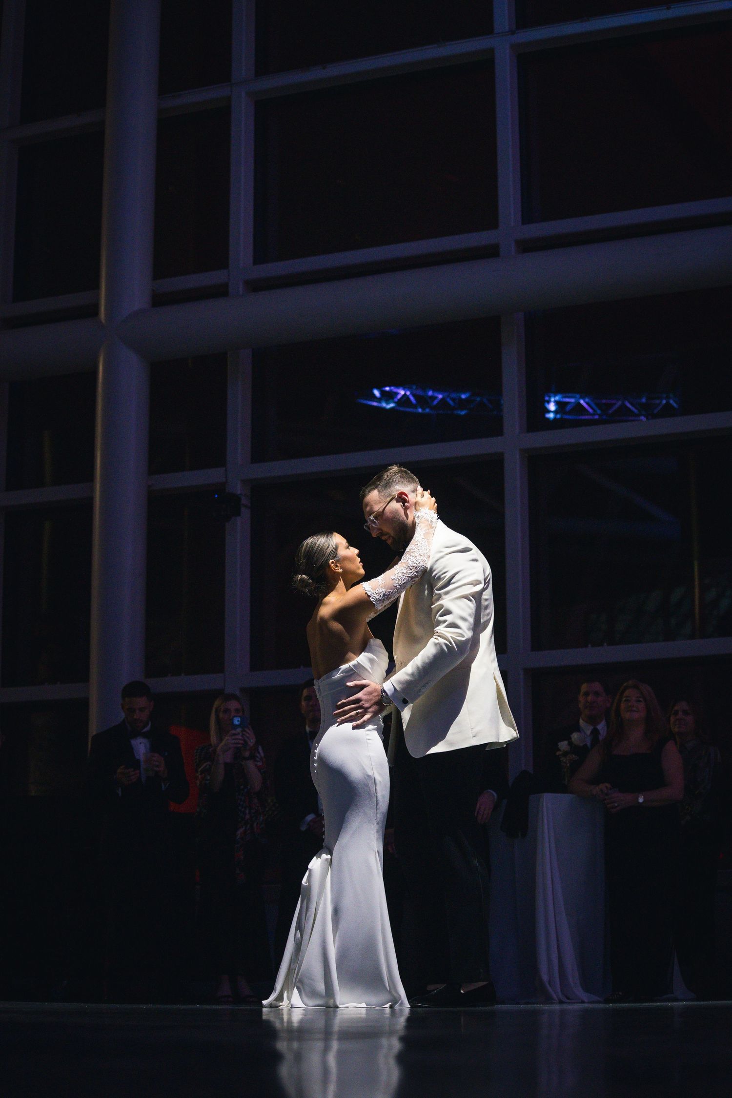Two dancers perform a romantic ballroom dance move in a white dress and formal attire.