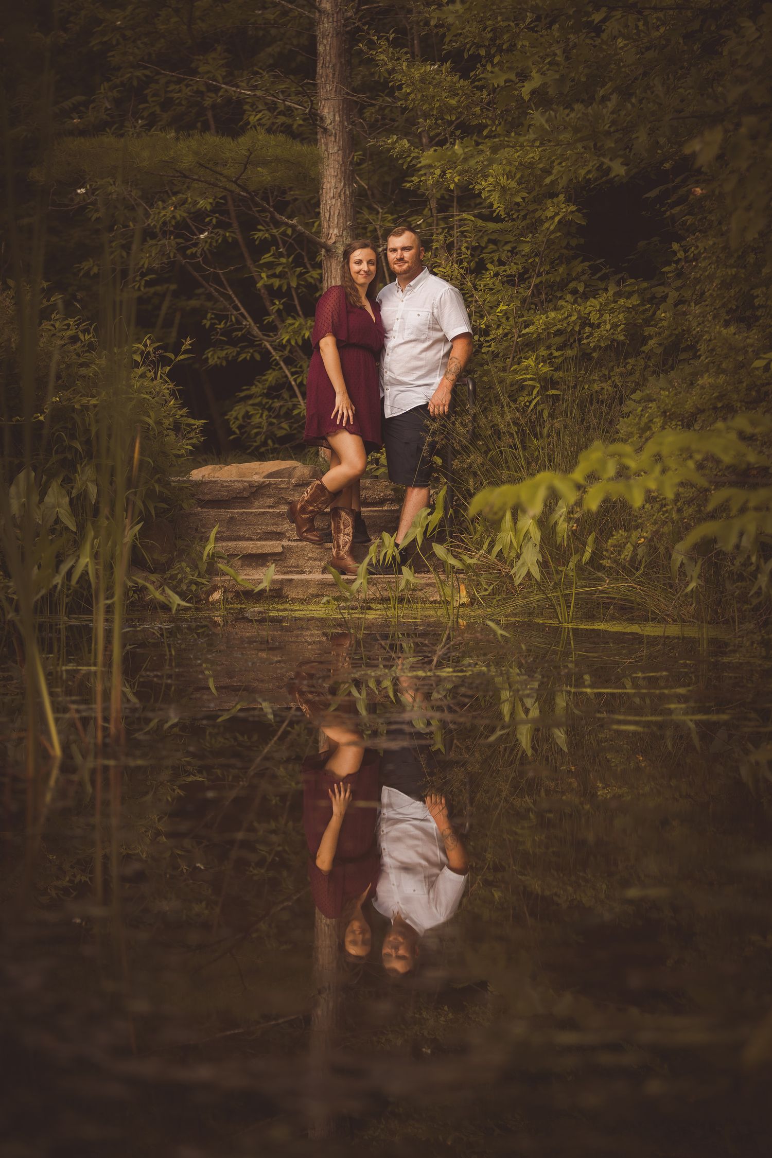 Two people sit on a dock with their reflection mirrored in the peaceful pond below.