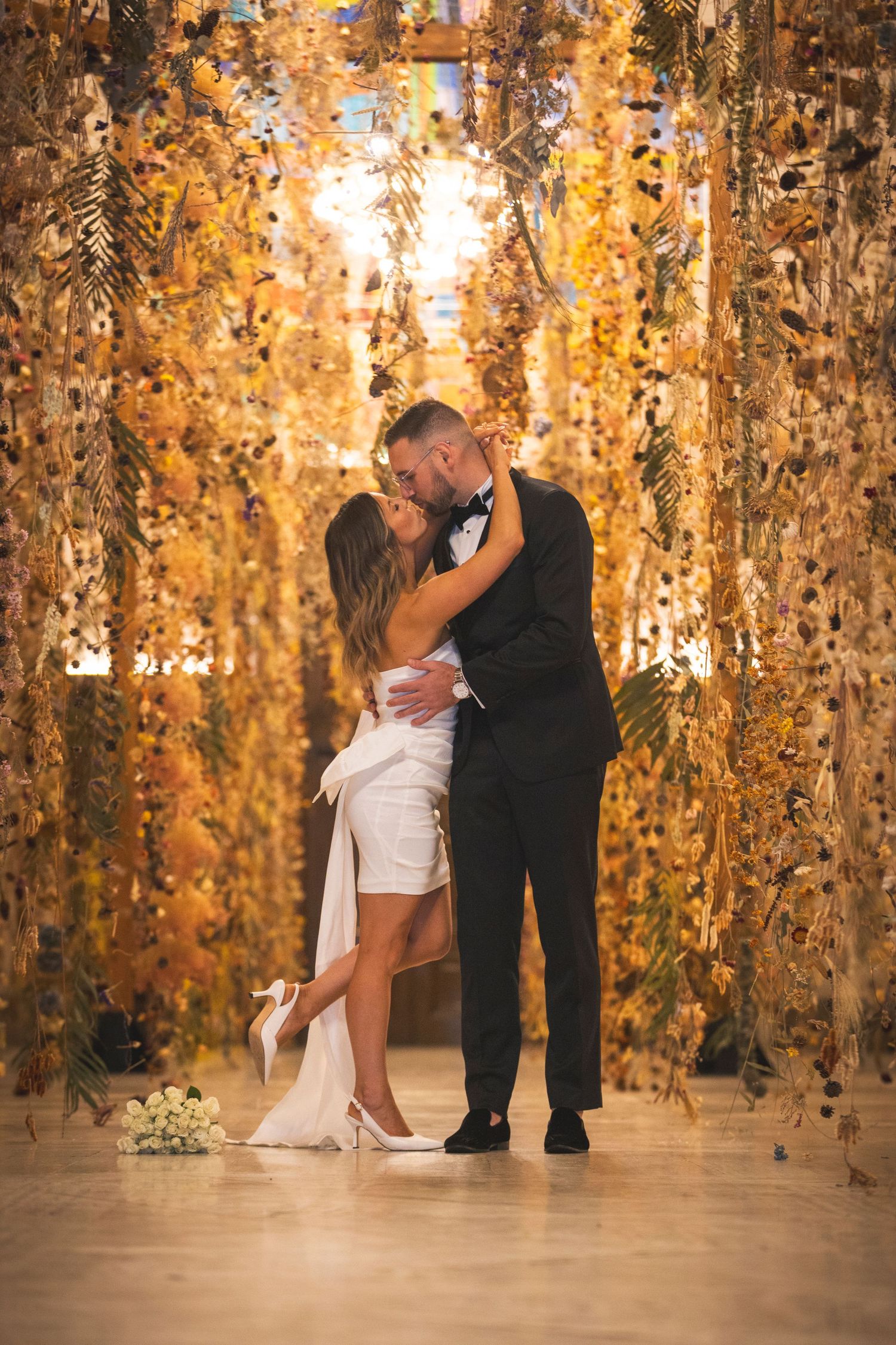 Couple sharing an intimate dance moment beneath hanging golden foliage decorations.