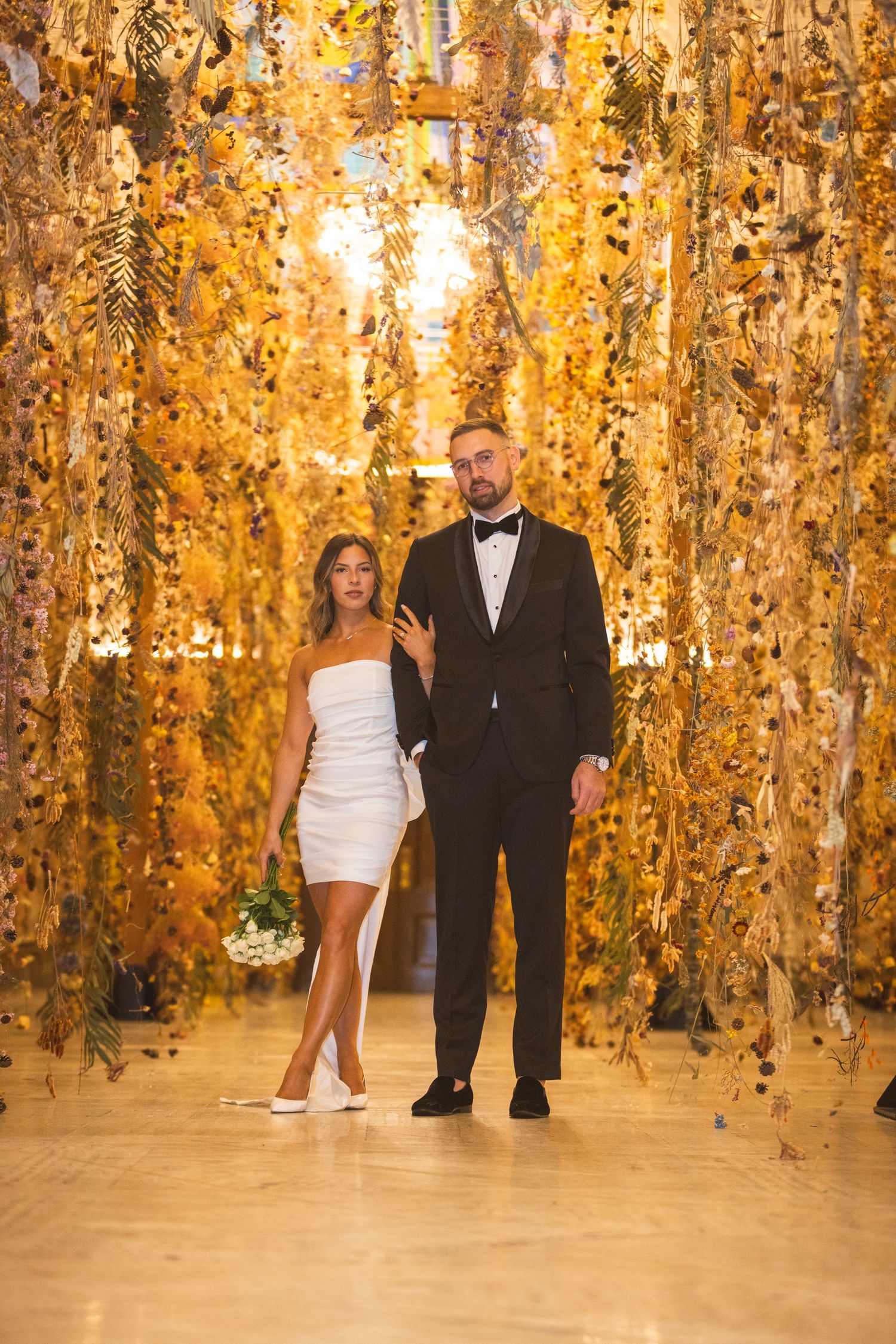 A couple walking through a stunning golden-lit corridor with hanging decorations.
