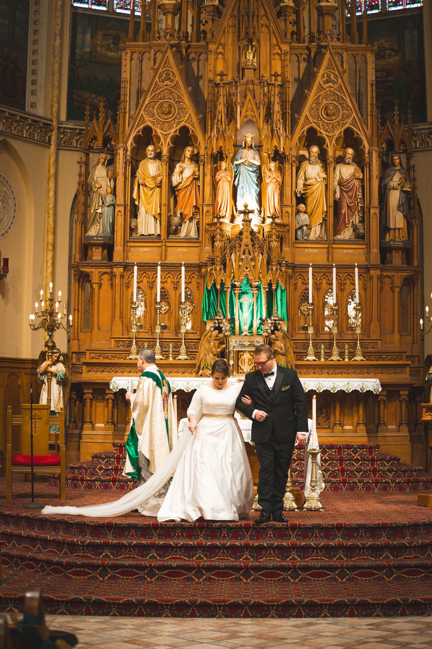 A wedding ceremony at the ornate altar of a gothic cathedral with gilded religious statues.