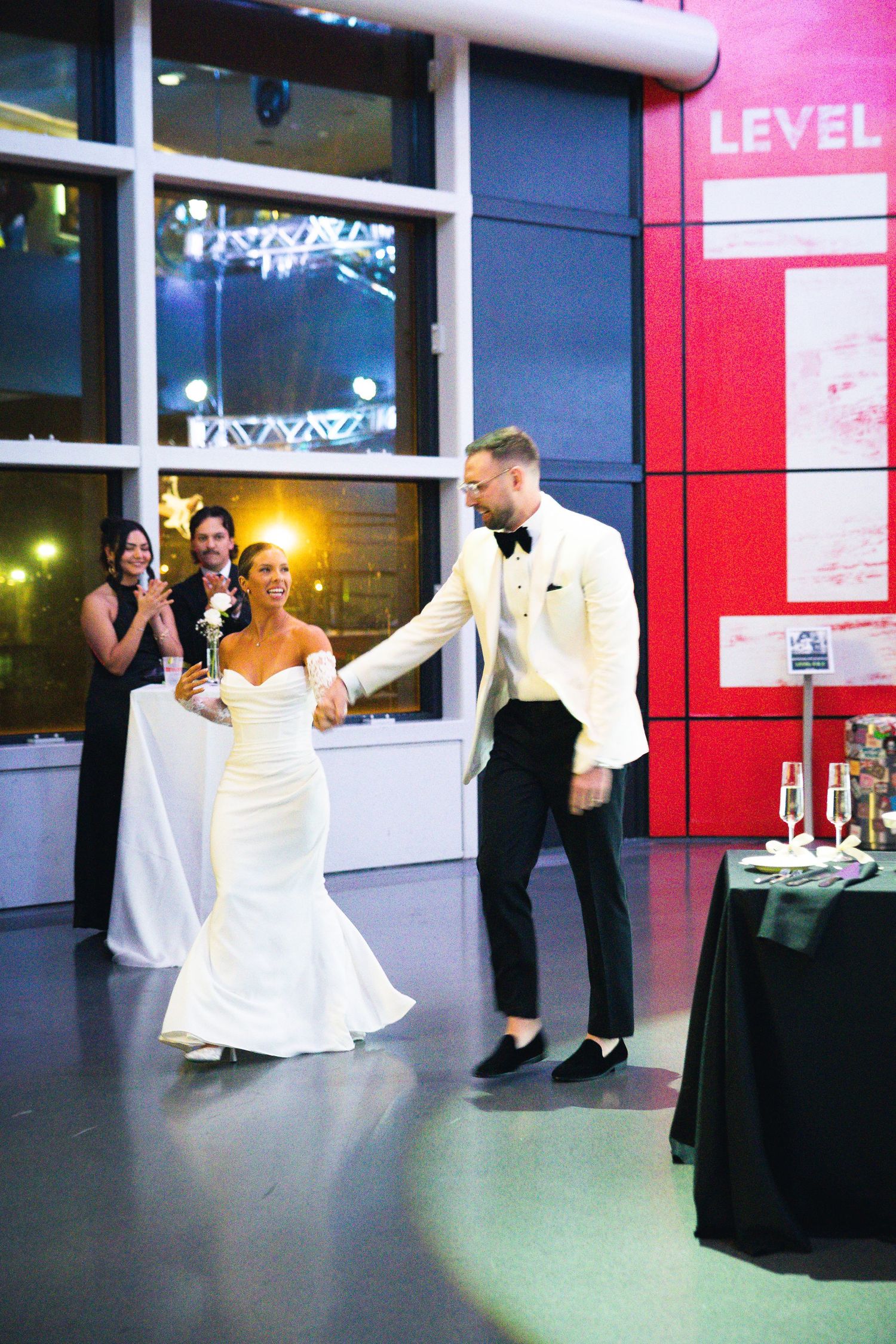 Wedding party celebrates at modern venue with red accent walls and white dress trailing.