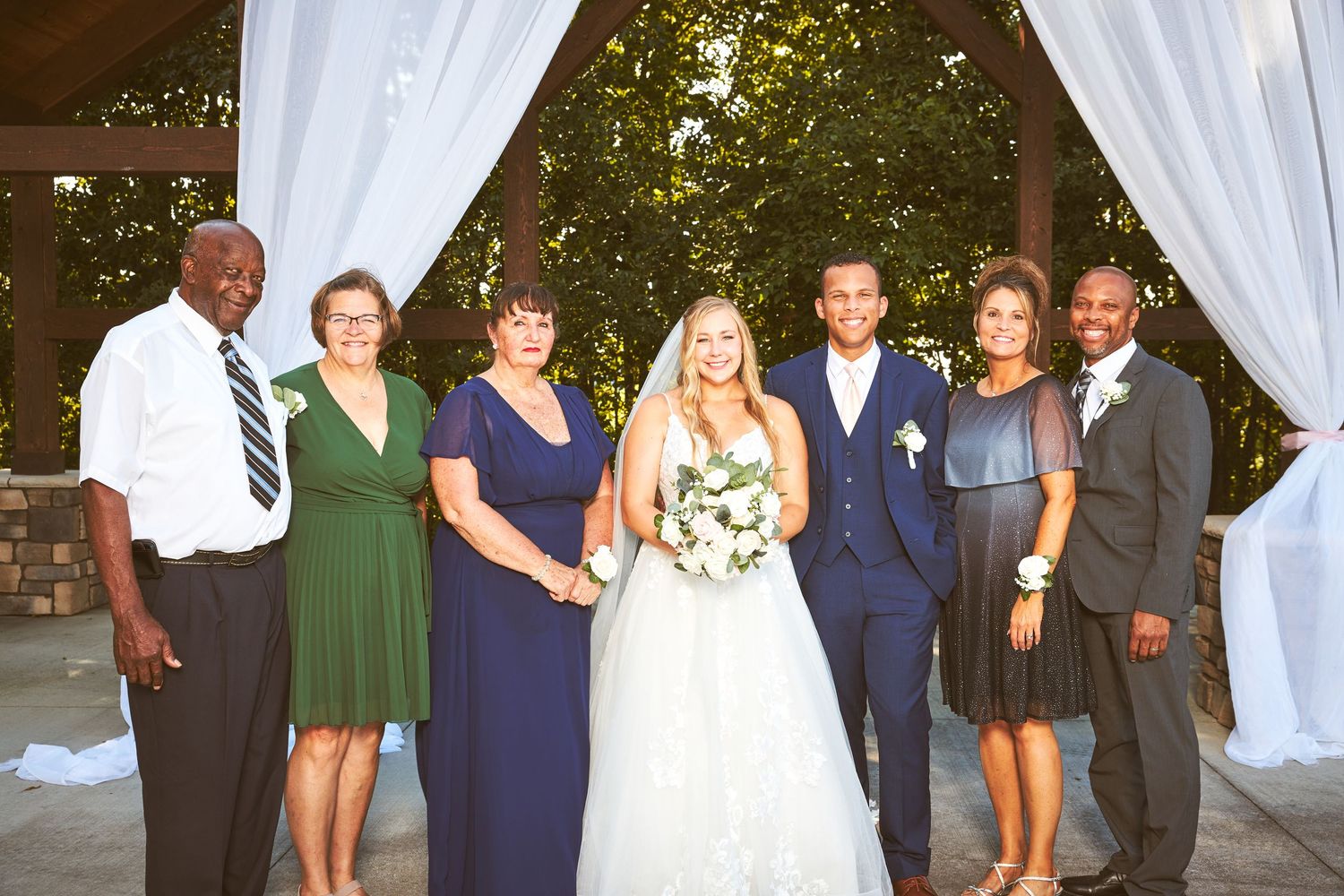 Wedding party members pose for formal photos at an outdoor venue.