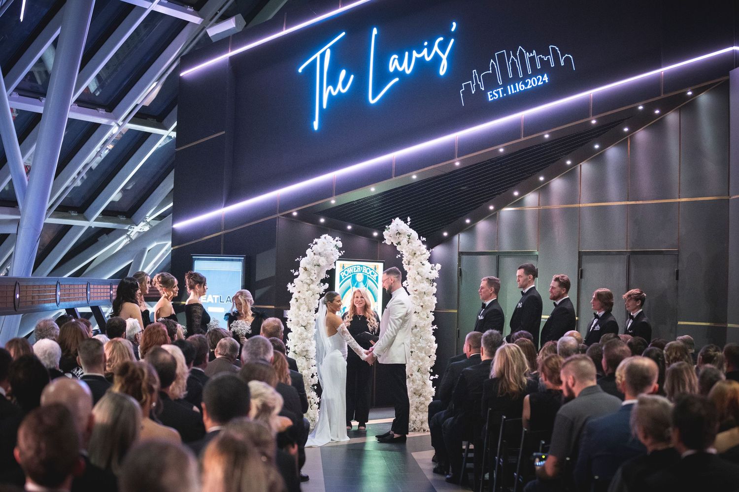 Wedding venue with modern blue neon lighting and white floral arrangements along the aisle.