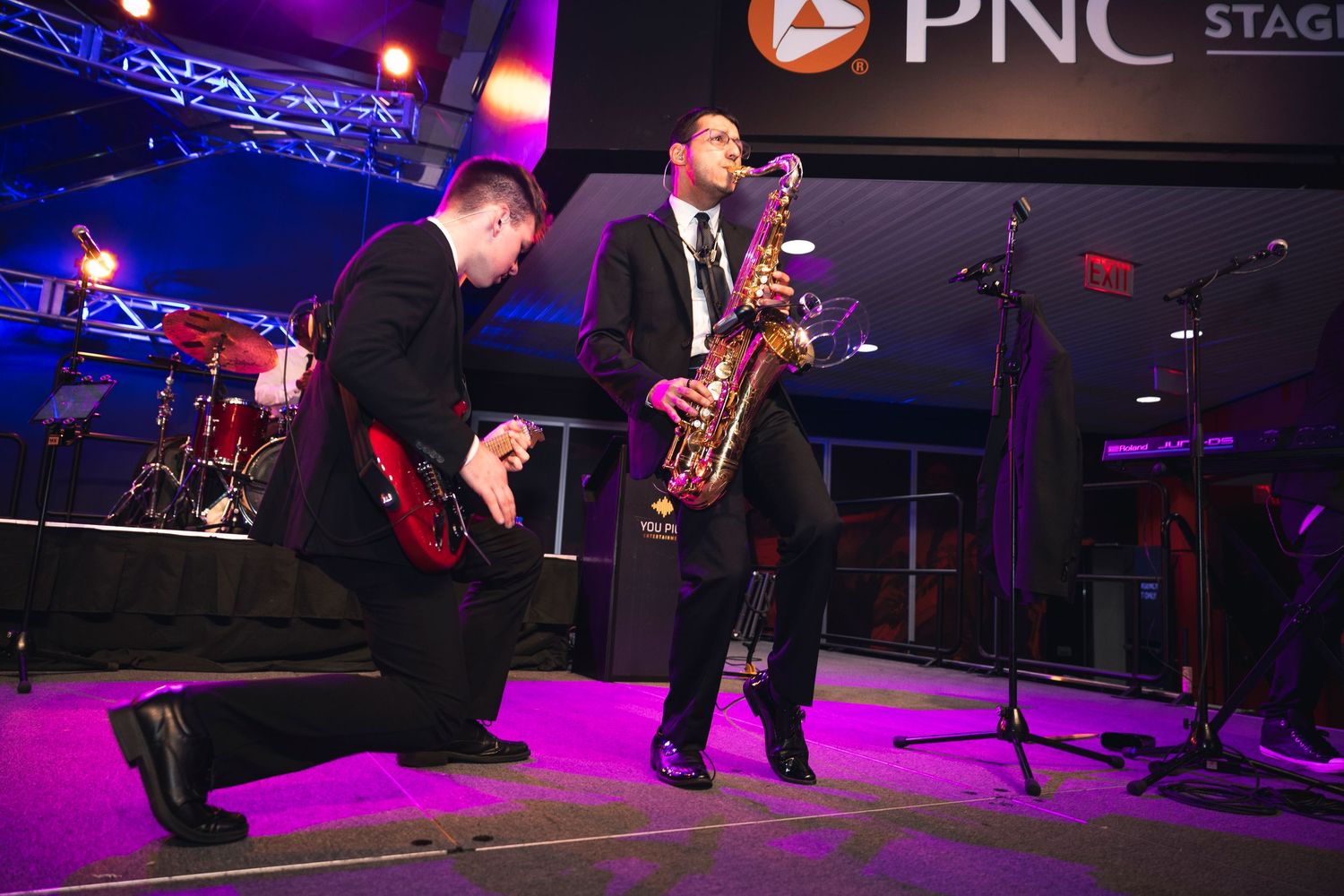 Live band performs on stage at PNC venue with dramatic purple lighting.