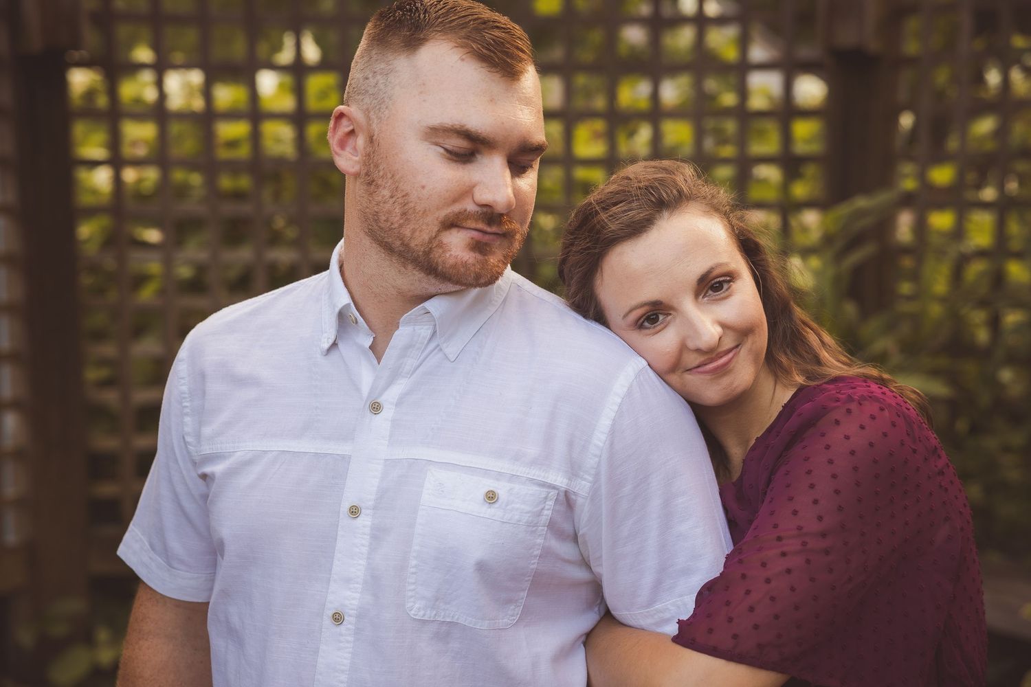Couple smiling and embracing in front of decorative garden trellis.