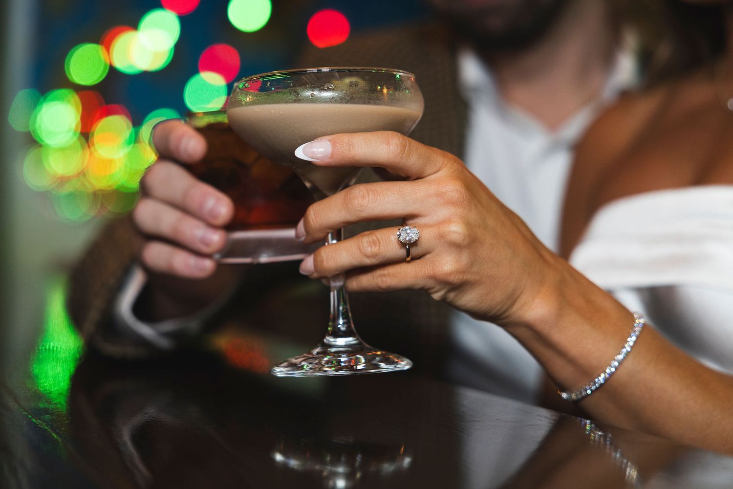 Elegant cocktail with foam topping held by hand with jewelry.