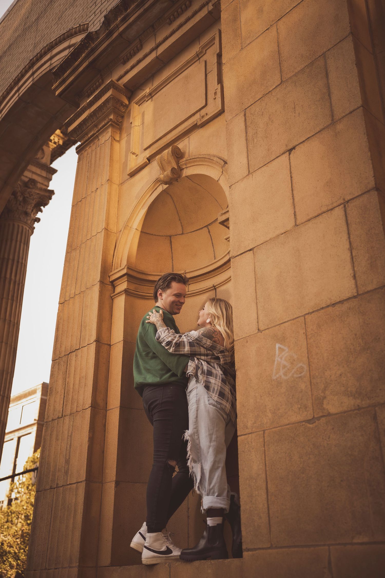 Golden hour sunlight illuminates classical stone archways and columns during intimate moment.