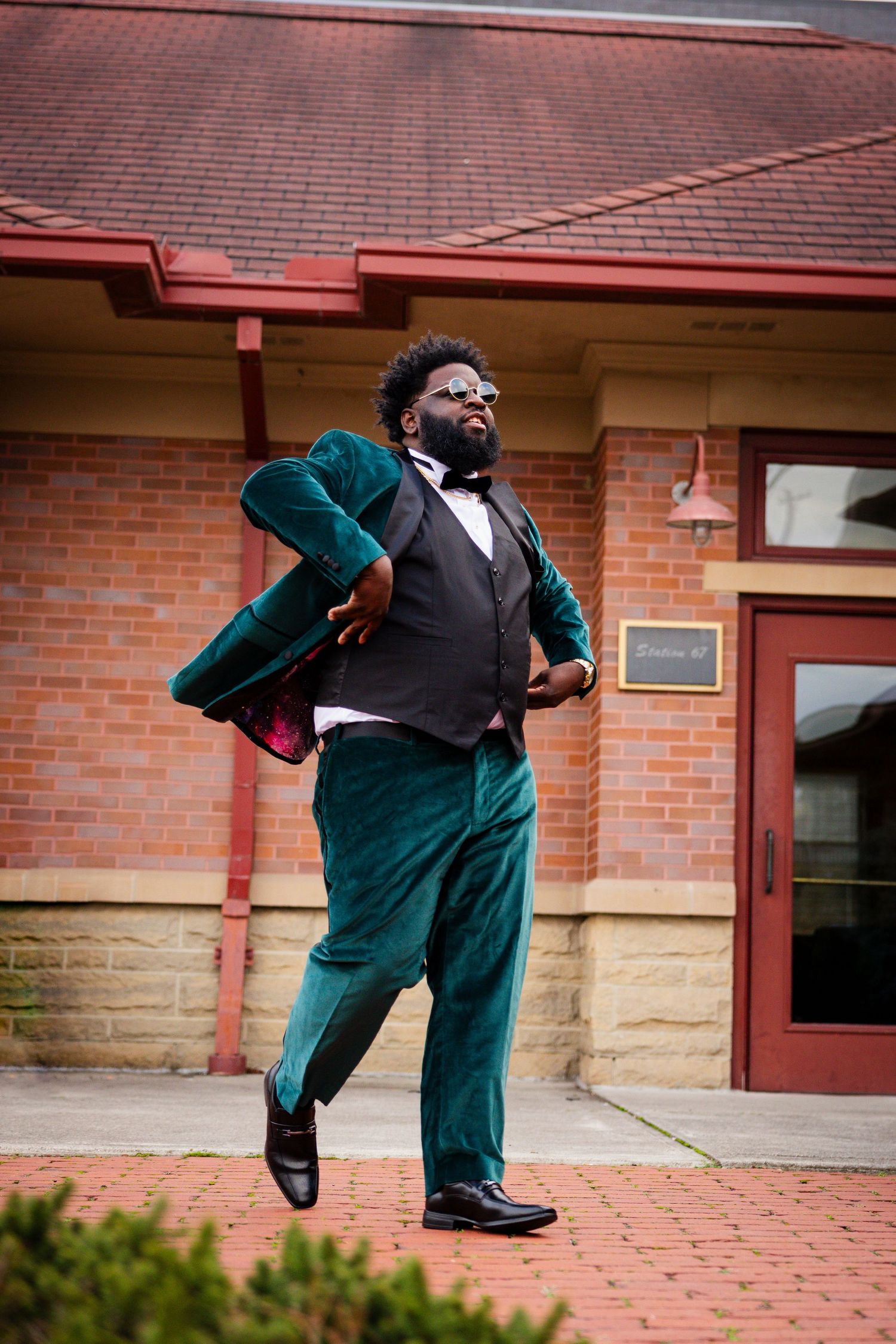 Dynamic dance poses in a green velvet suit captured against a brick building backdrop.