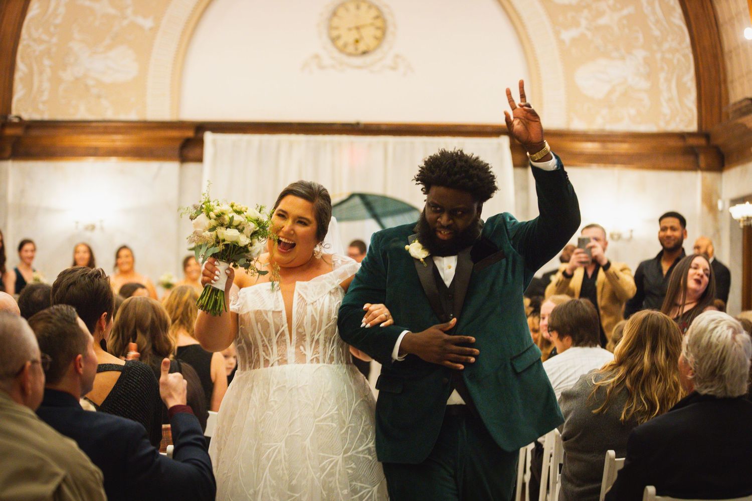 Wedding guests celebrate on a dance floor under ornate ceiling decorations.