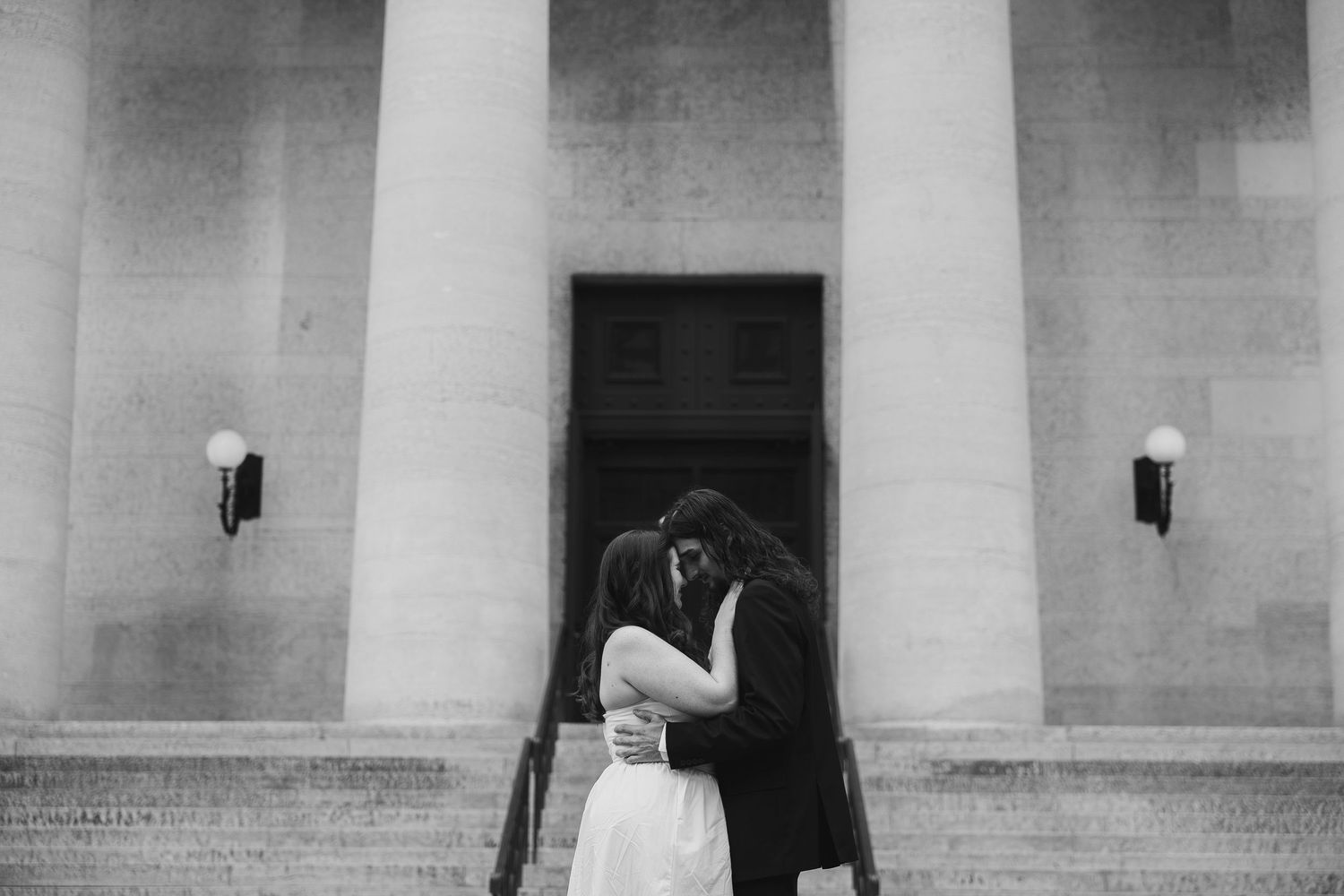 Two people pose playfully between stone pillars during a formal photo session.