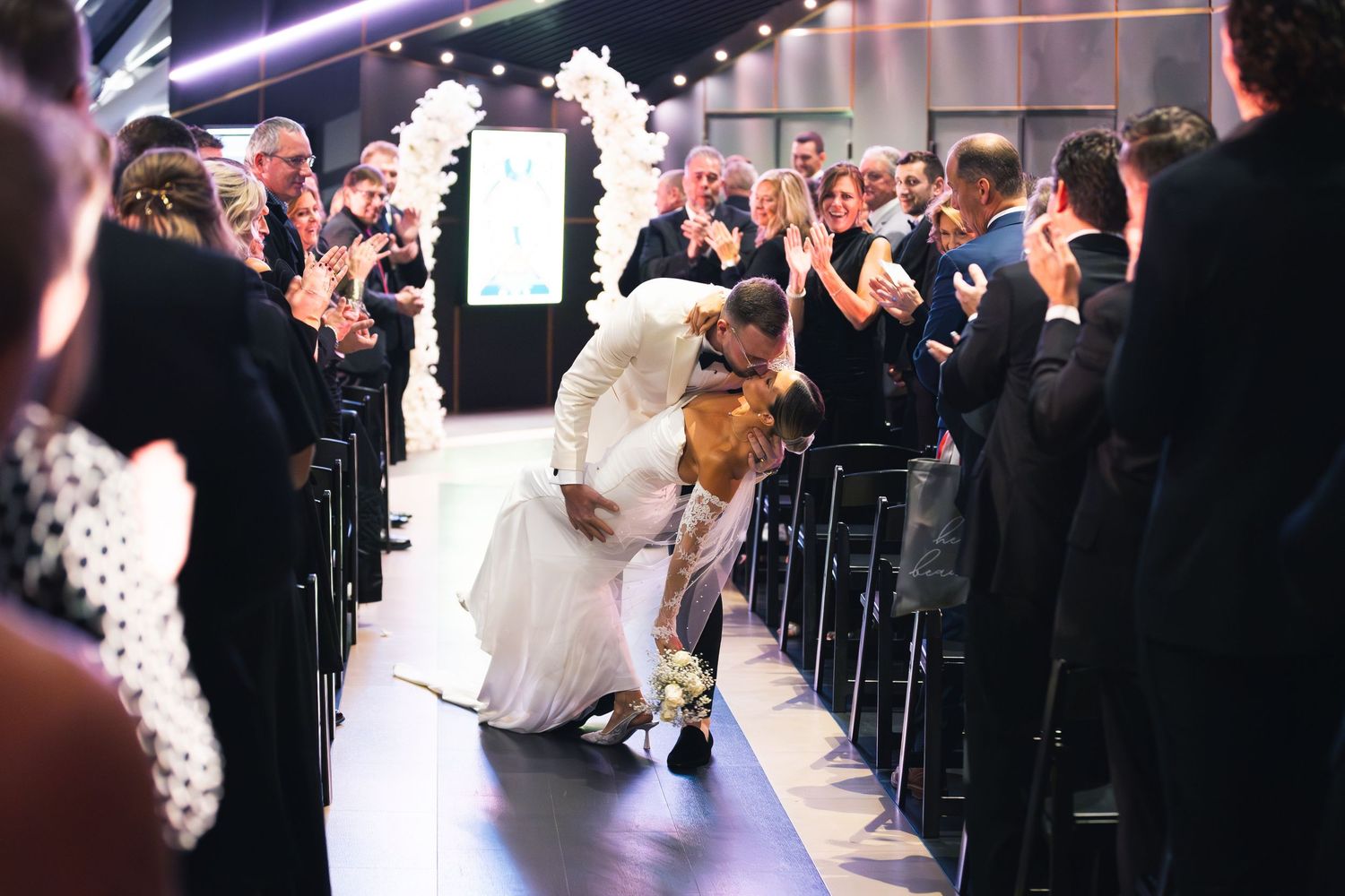 Wedding ceremony with elegant white floral arrangements and dramatic lighting.