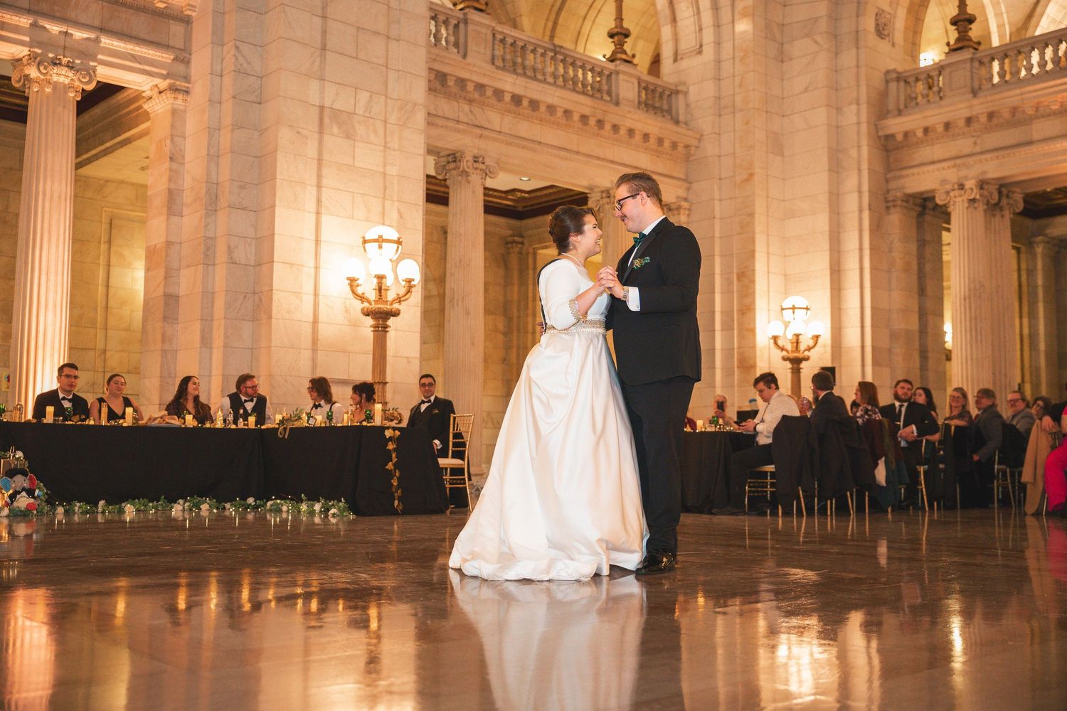 Grand ballroom with ornate columns and chandeliers set up for an elegant wedding celebration.