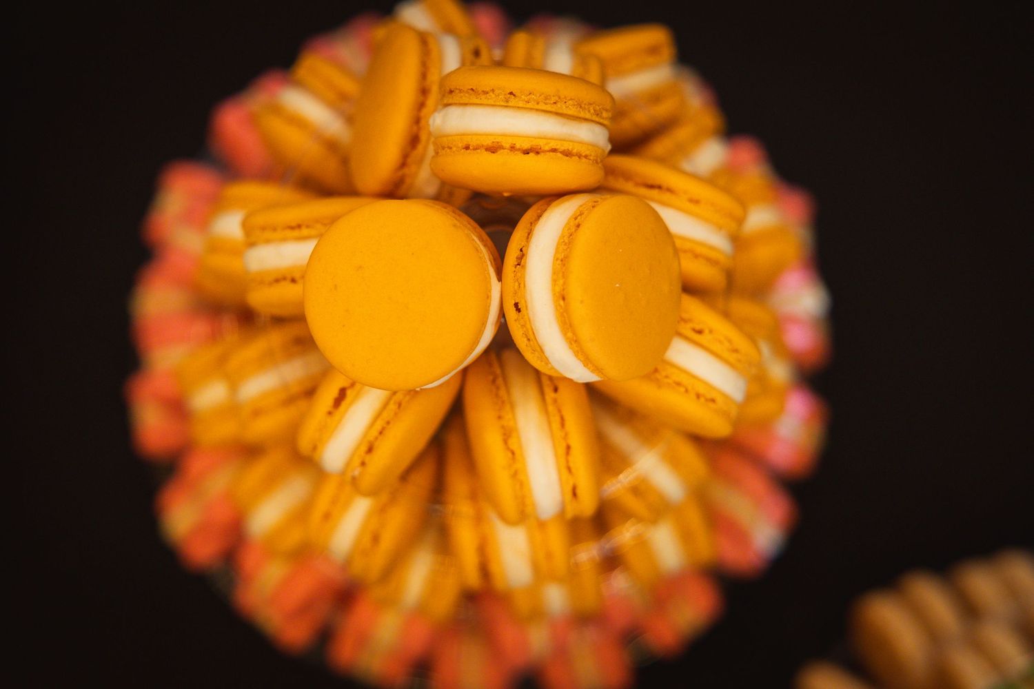 Orange and coral-colored macarons arranged in a circular pattern against a dark background.
