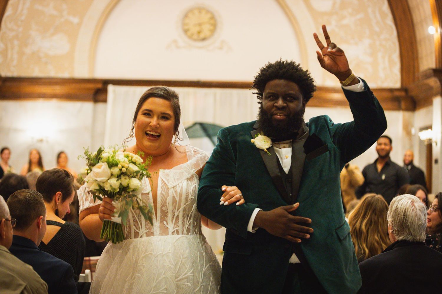 Wedding party celebrates joyfully in front of a classic brick building on a festive evening.