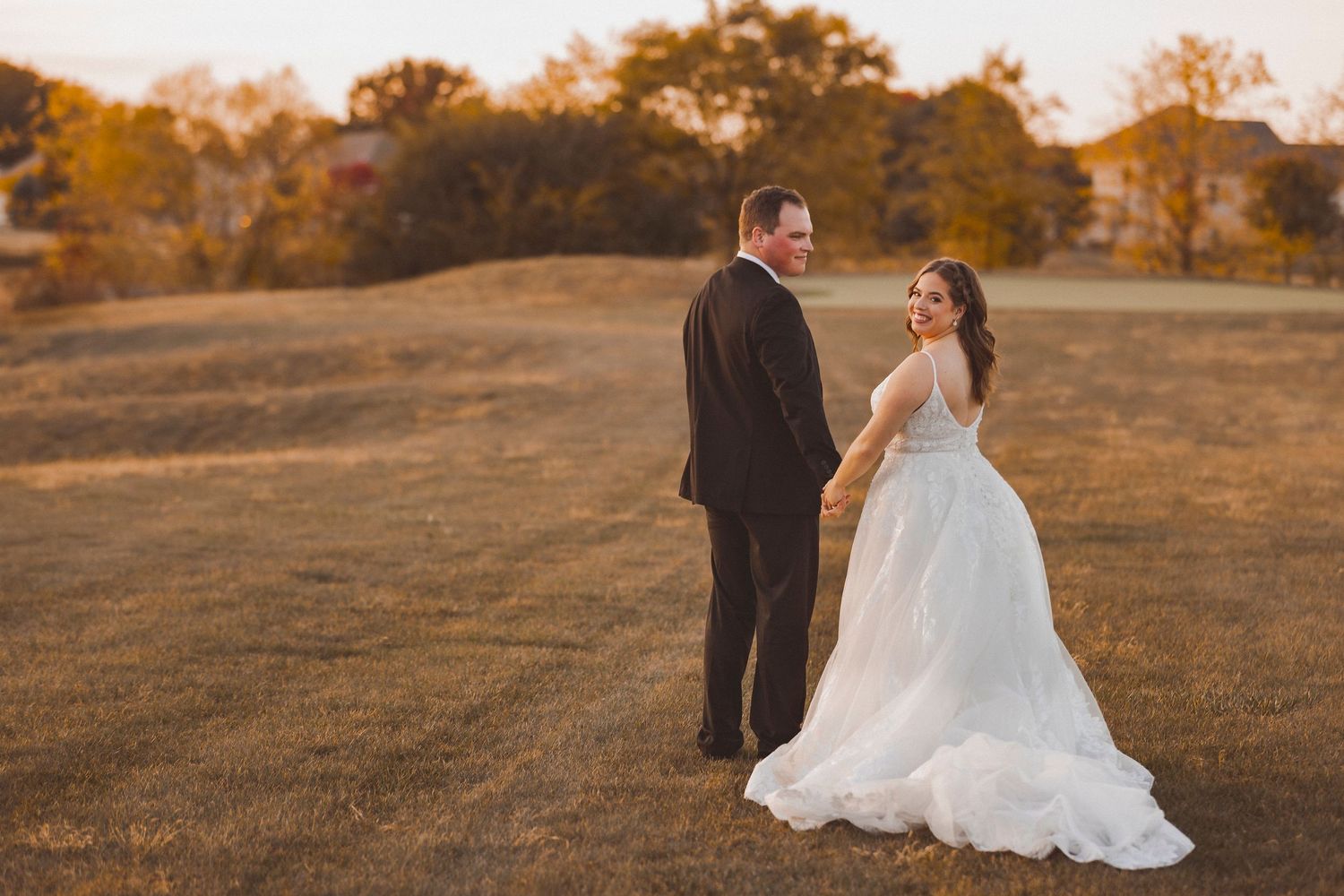Couple in wedding attire embraces during golden hour sunset in a scenic outdoor setting.