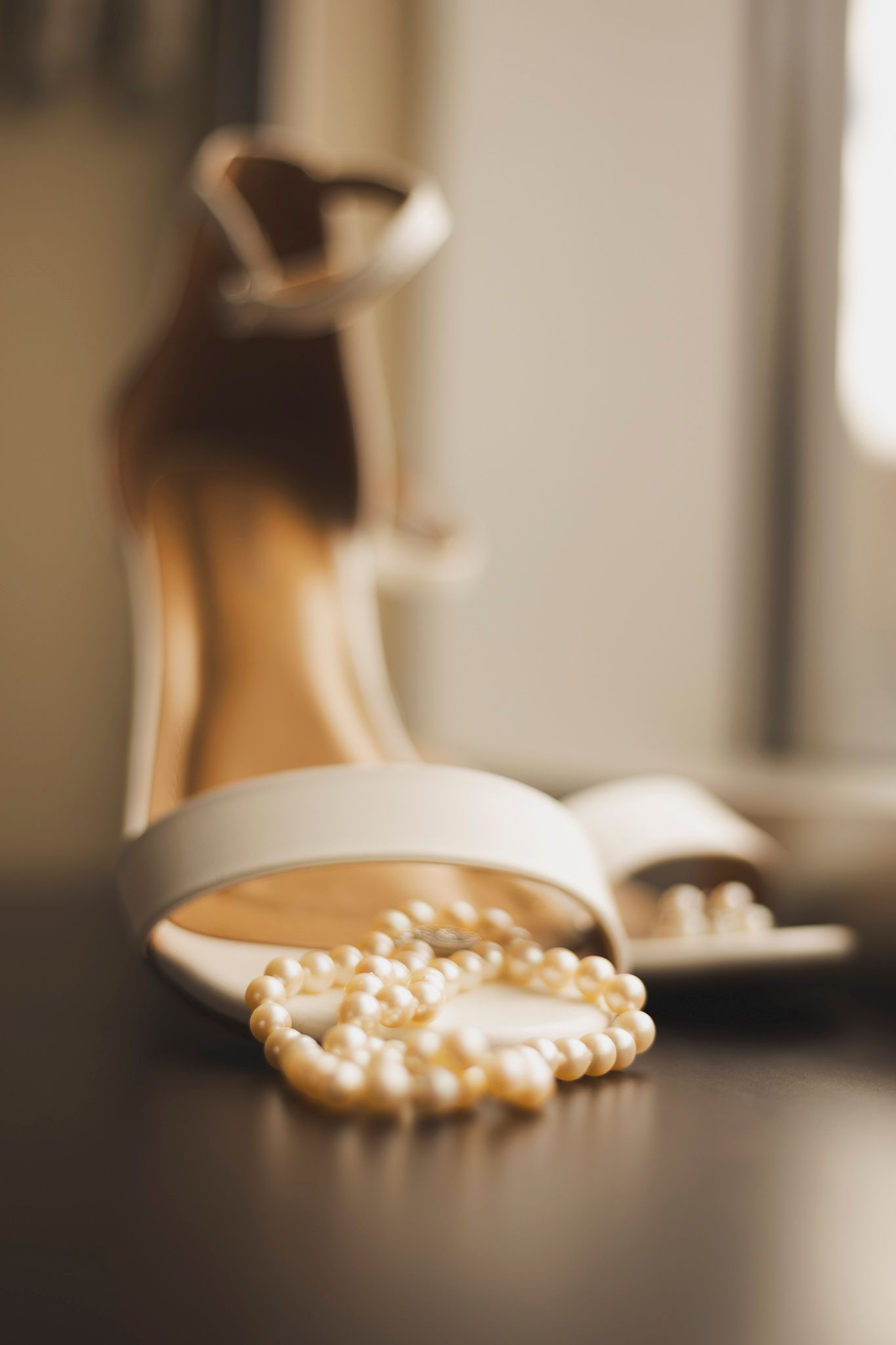 Pearl beaded wedding shoes sitting on a dark surface in soft focus.