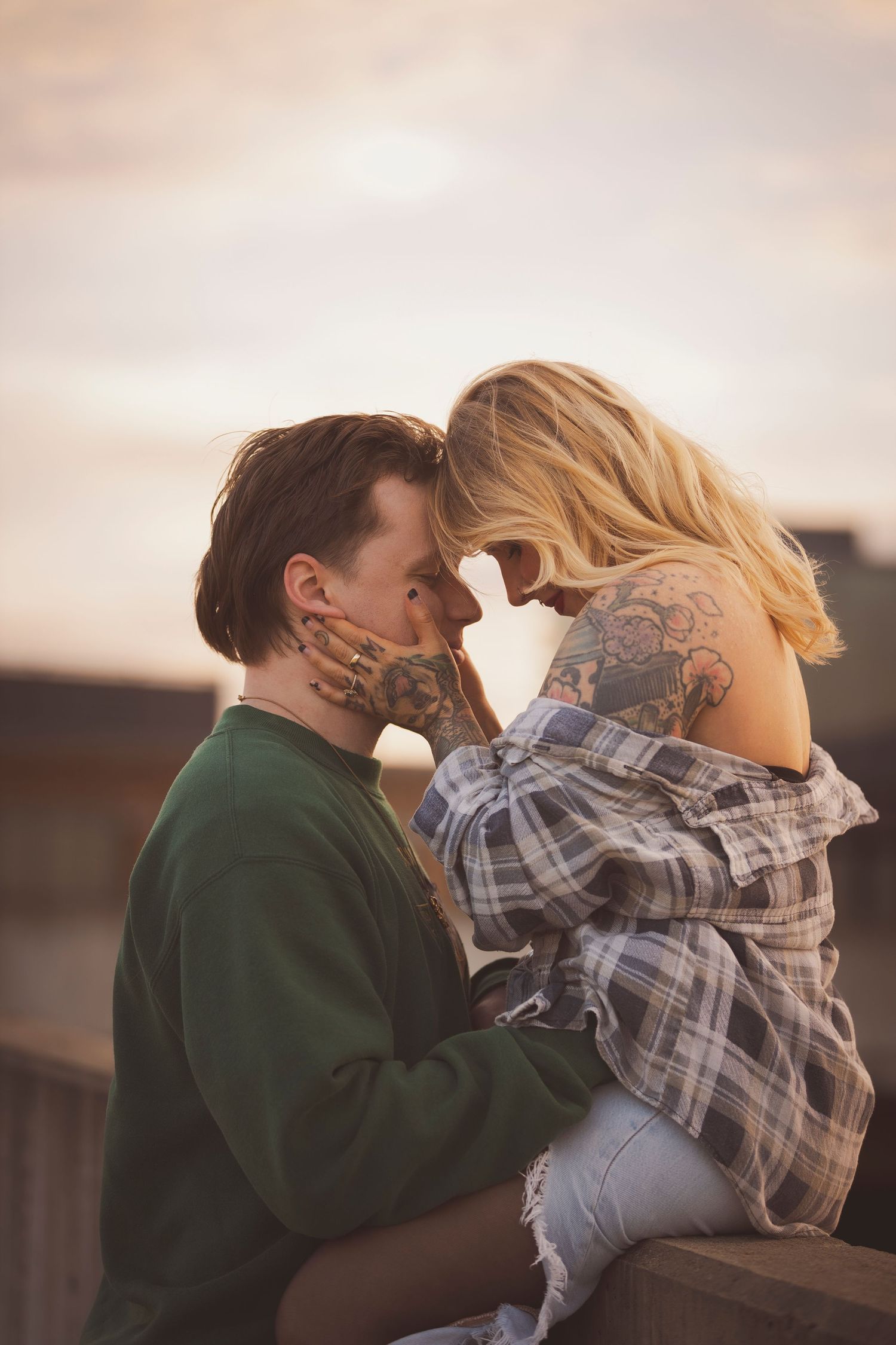 Romantic couple in plaid and green embracing against warm sky.