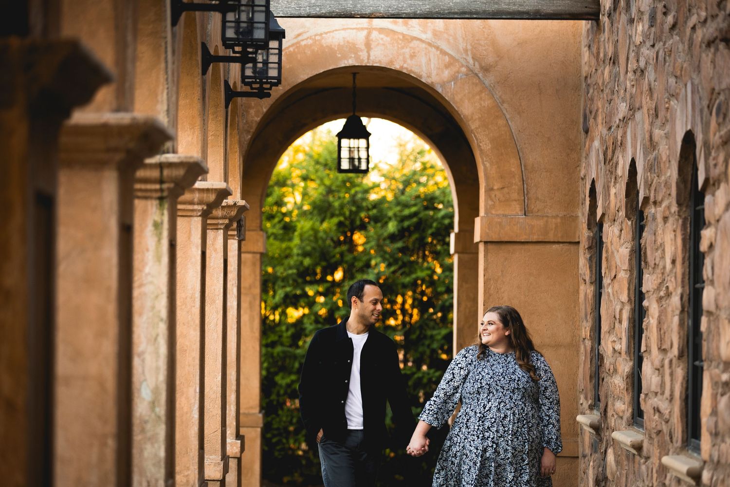 A couple walks through a covered stone colonnade during golden hour.