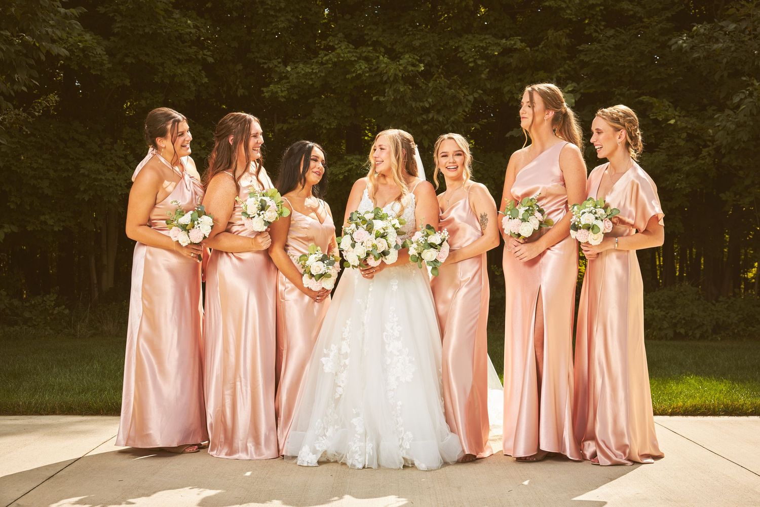 Bridesmaids in blush pink gowns gather for a group photo outdoors.