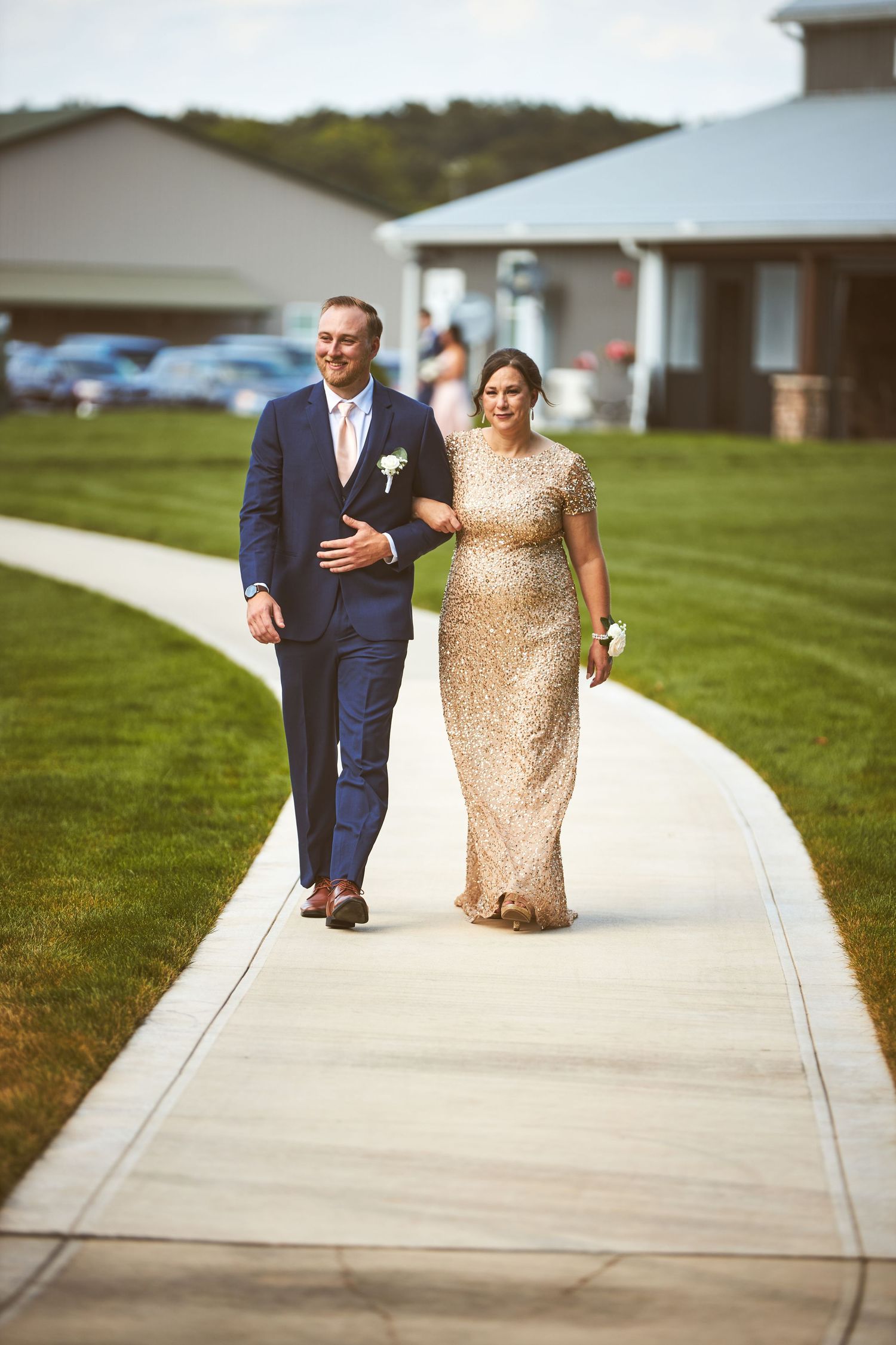 Couple in formal attire walks together on a concrete pathway.